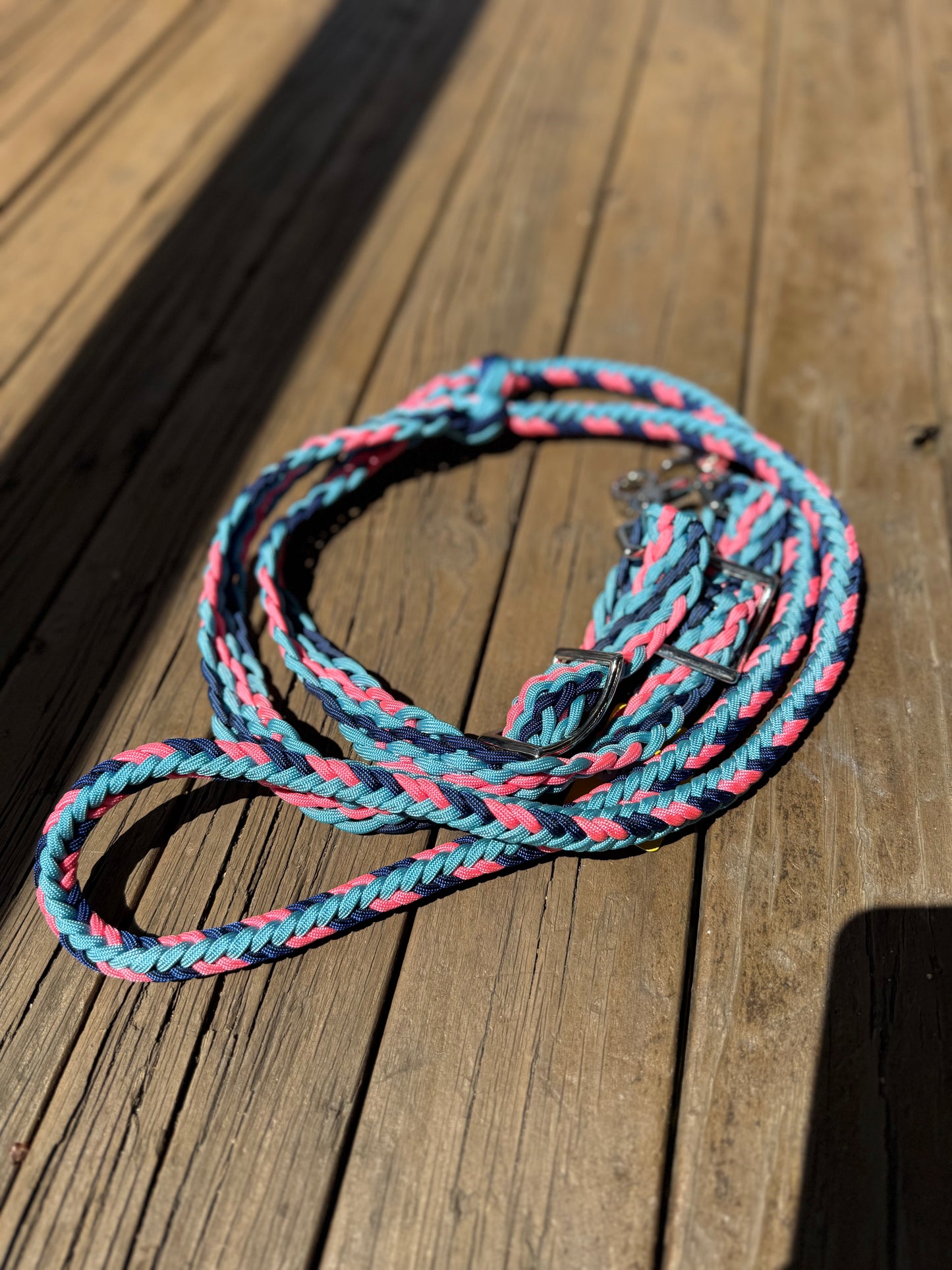 Standard length braided reins in Carolina blue, navy, and pink nylon cord, featuring round and flat braid sections with Conway buckles and trigger snap ends.