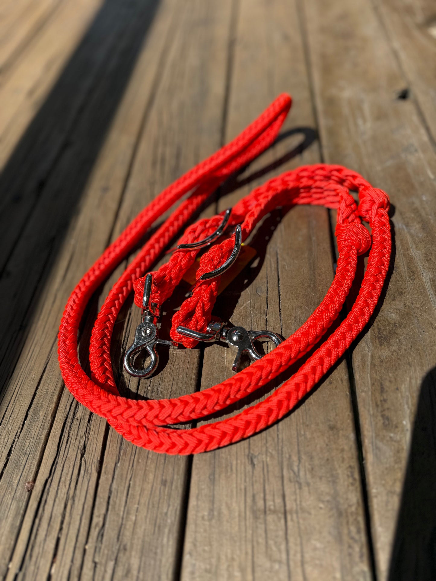 A set of bright orange, hand-braided barrel racing reins laid out on a wooden surface.