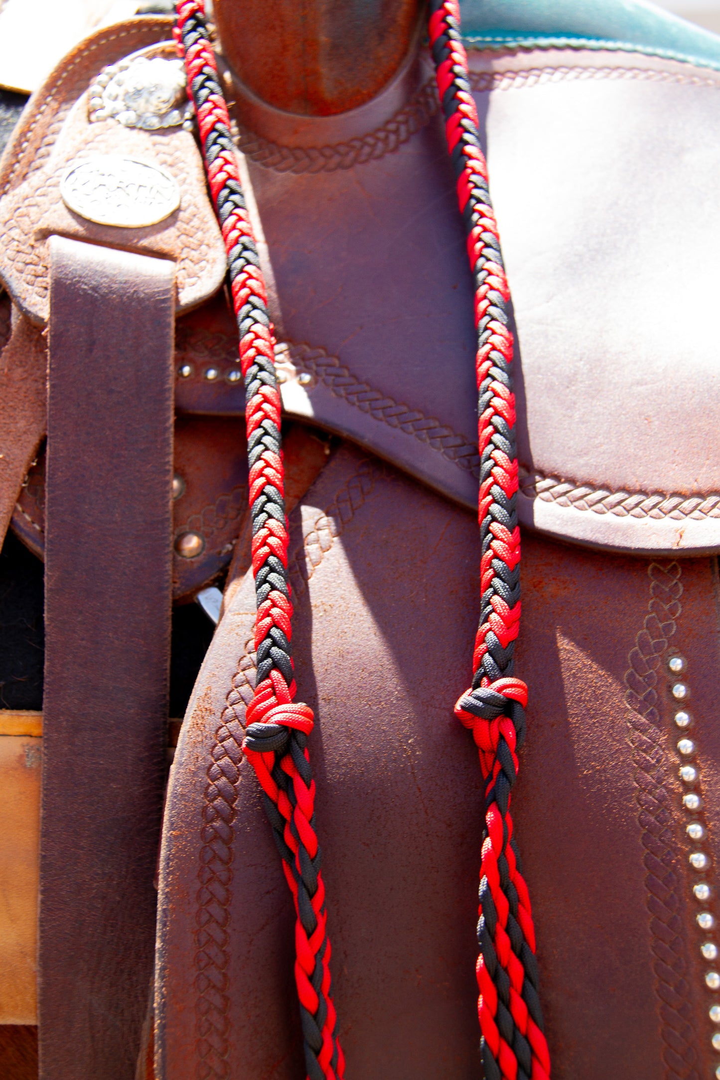 Close-up of a brown leather saddle with red and black braided reins.