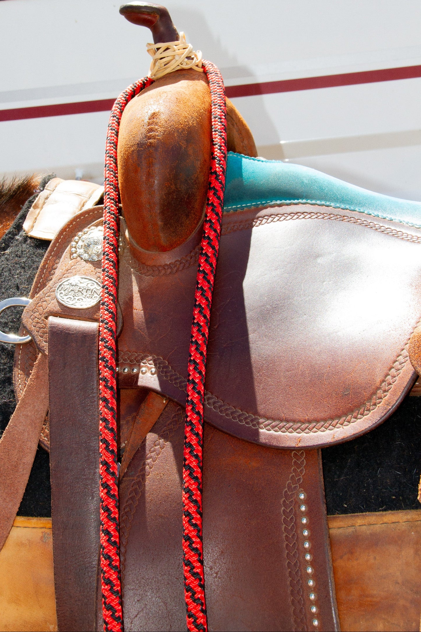 Close-up of a horse saddle with a red braided reins against a blurred background