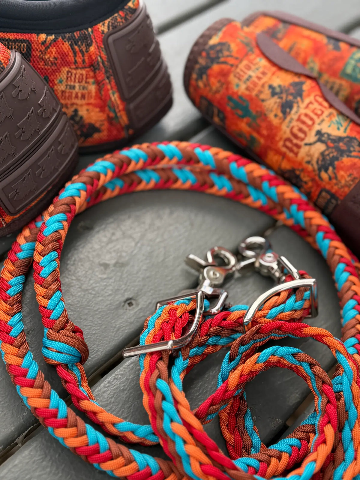 Detailed view of rust brown, red, orange and turquoise stabiliser reins and fittings beside 8 Seconds horse boots