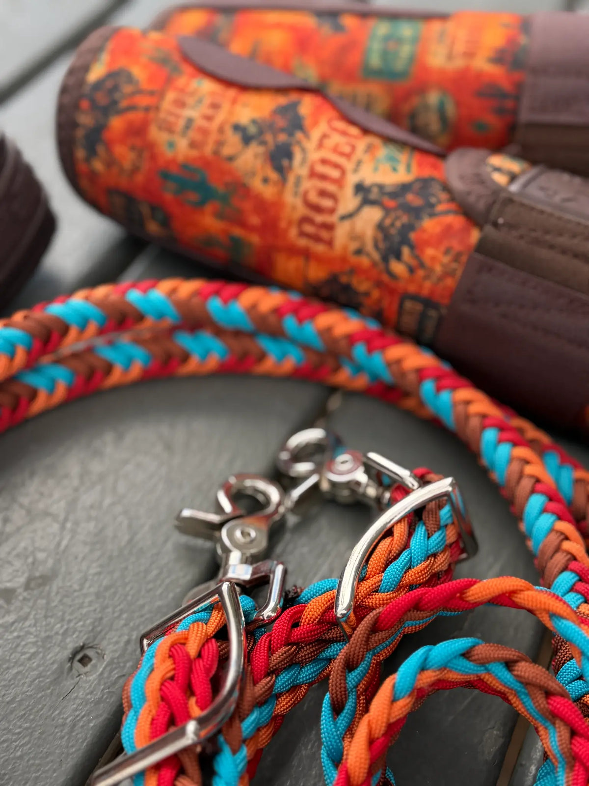 Close-up of 8 Seconds colourway stabiliser reins showing rust brown, red, orange and turquoise braiding, conway buckles and trigger snaps