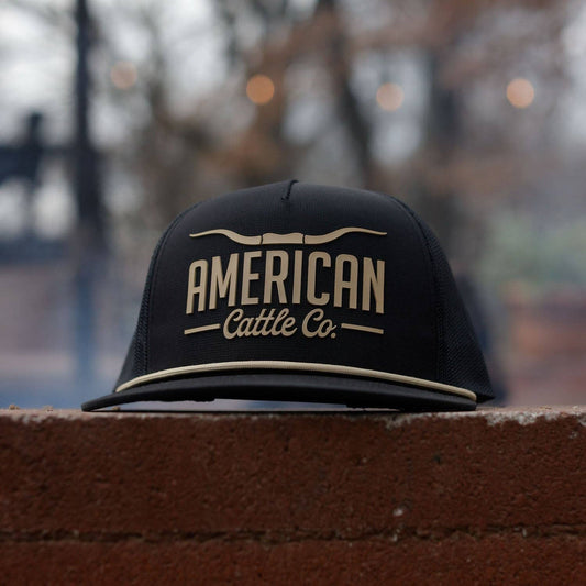 Black cap with 'American Cattle Co.' text on a brick ledge with a blurred background