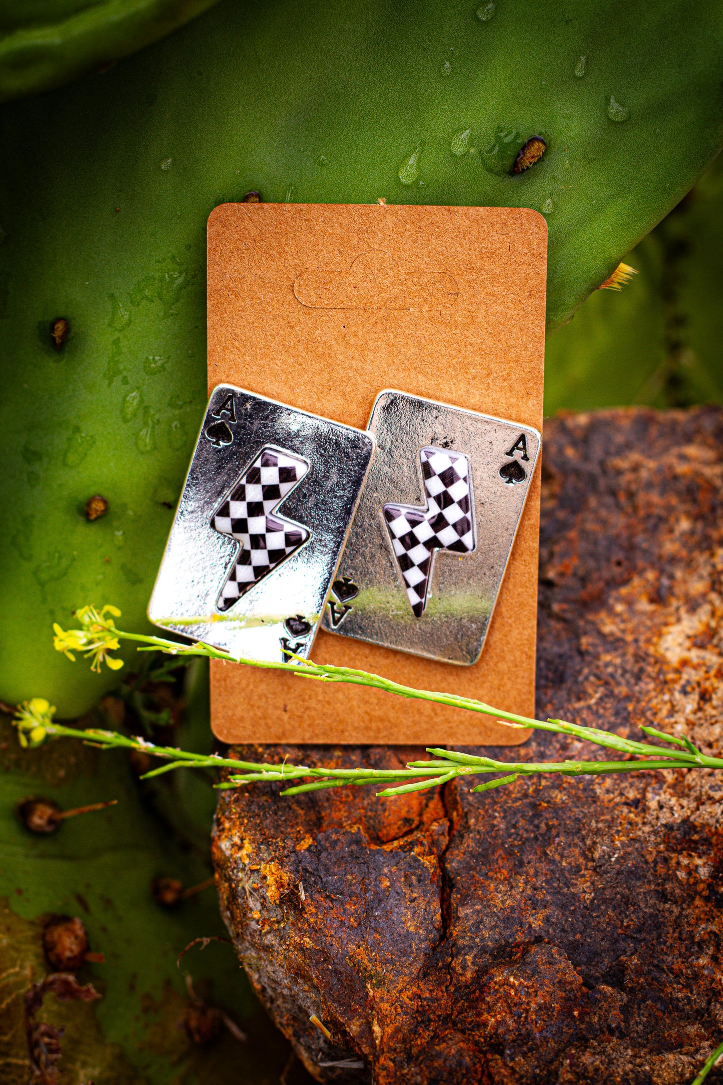 Pair of silver playing card-shaped earrings on a brown card with a natural background