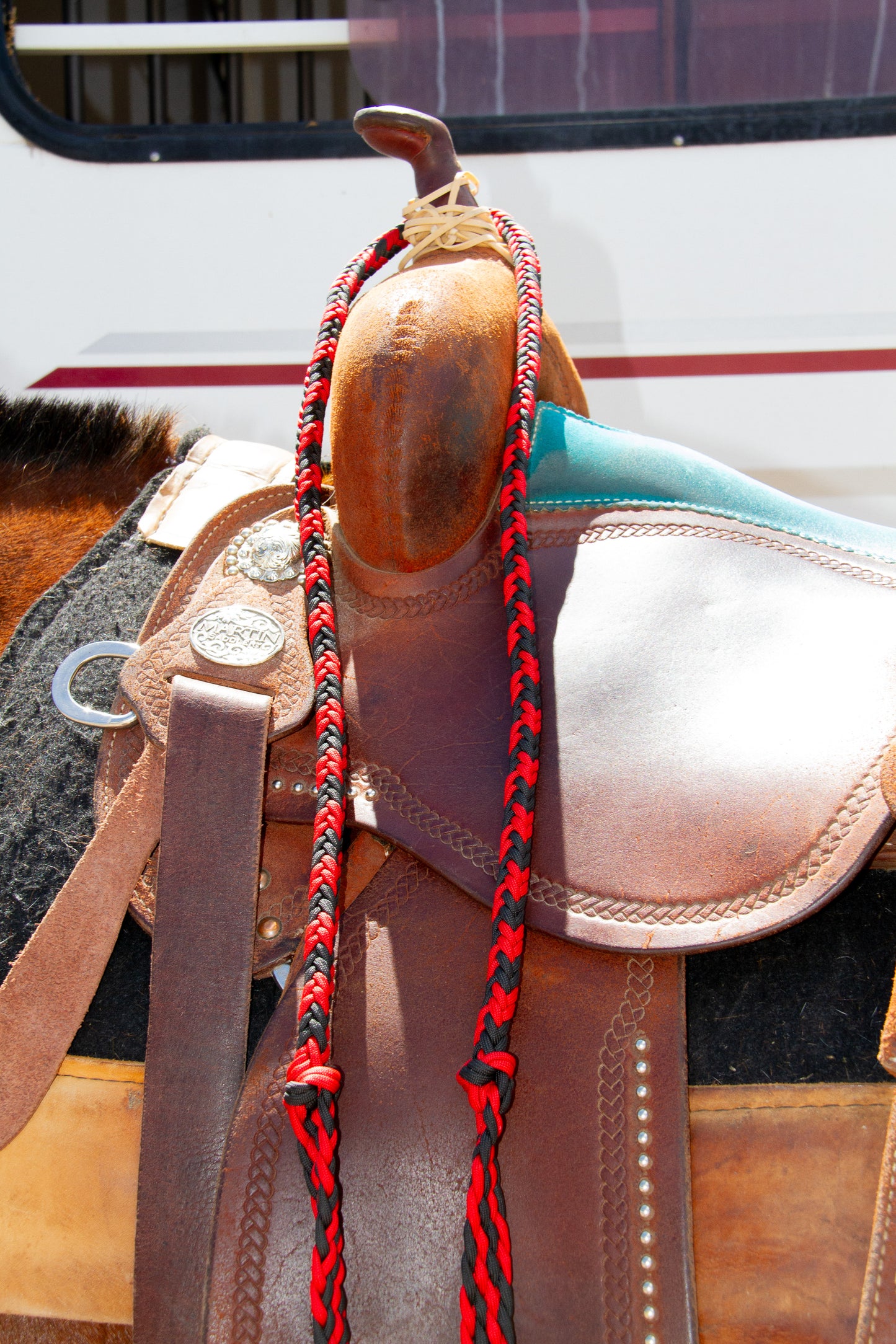 Close-up of a horse saddle with a red and black braided reins on a blurred background