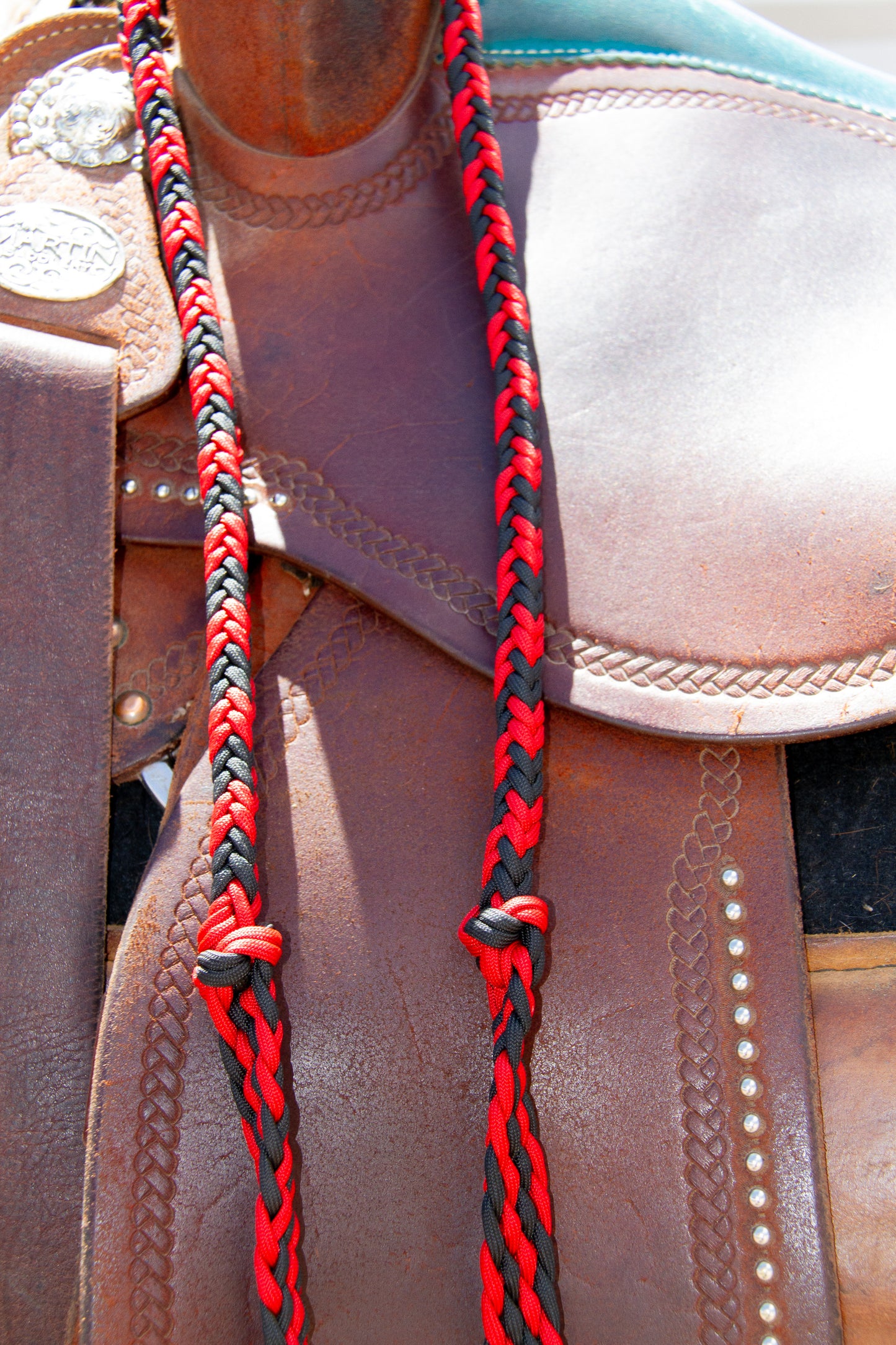 Close-up of a leather saddle with red and black braided reins.