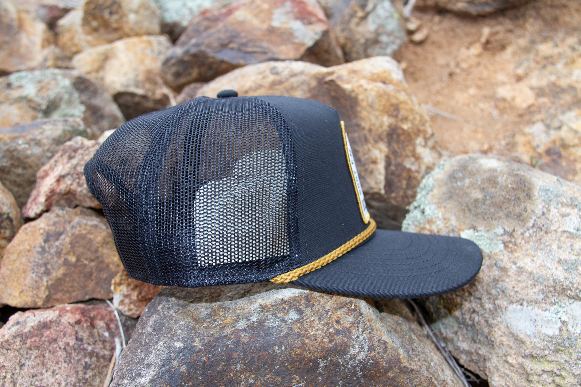 Black mesh cap with gold trim on a rocky surface