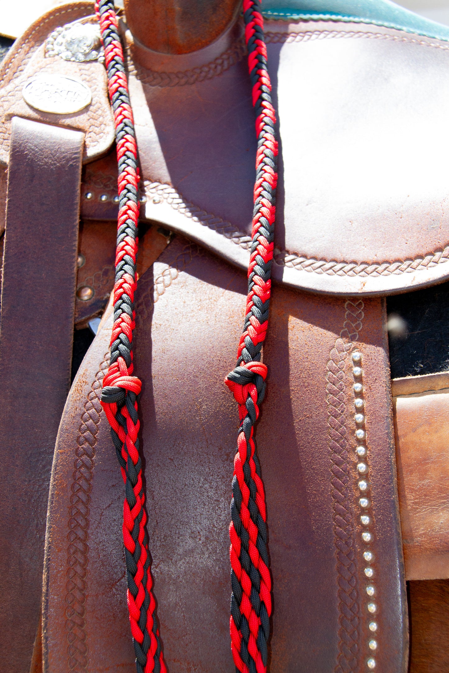 Close-up of a leather saddle with red and black braided reins.