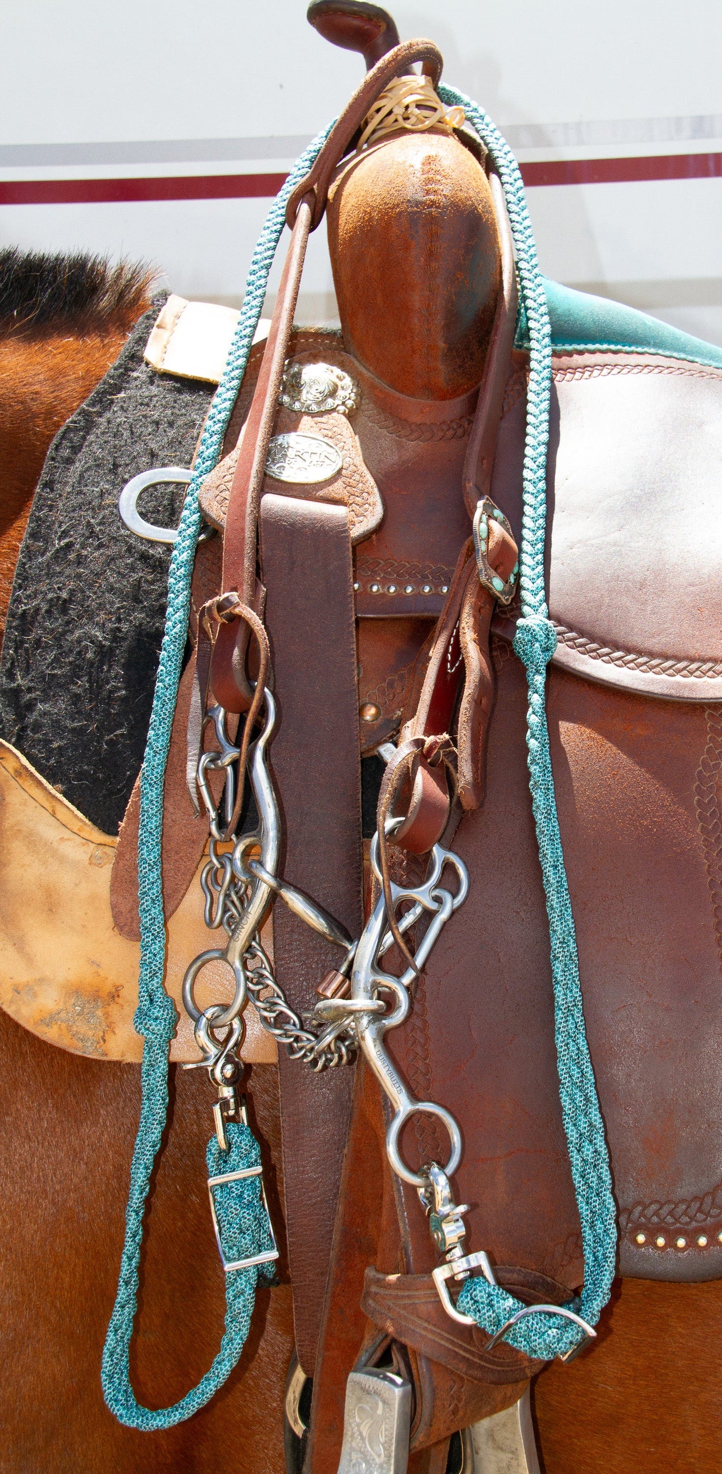 Close-up of a brown leather saddle with turquoise reins and hardware on a horse.