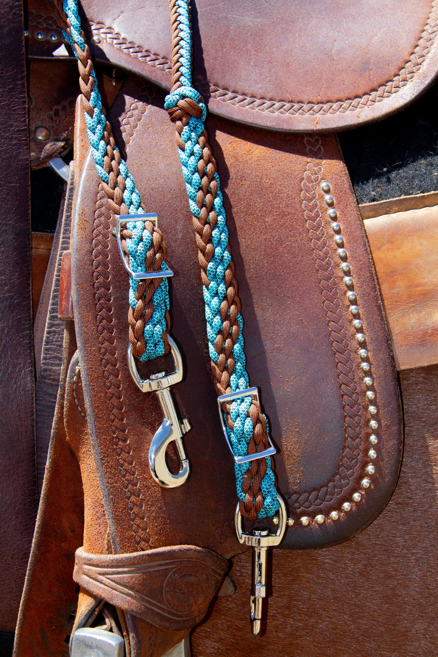 Close-up of a brown leather saddle with turquoise reins and hardware.