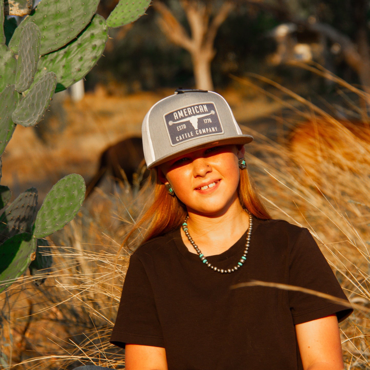 Person wearing Bull Spurs Flat Bill Snapback Hat sitting among cacti and dry grass