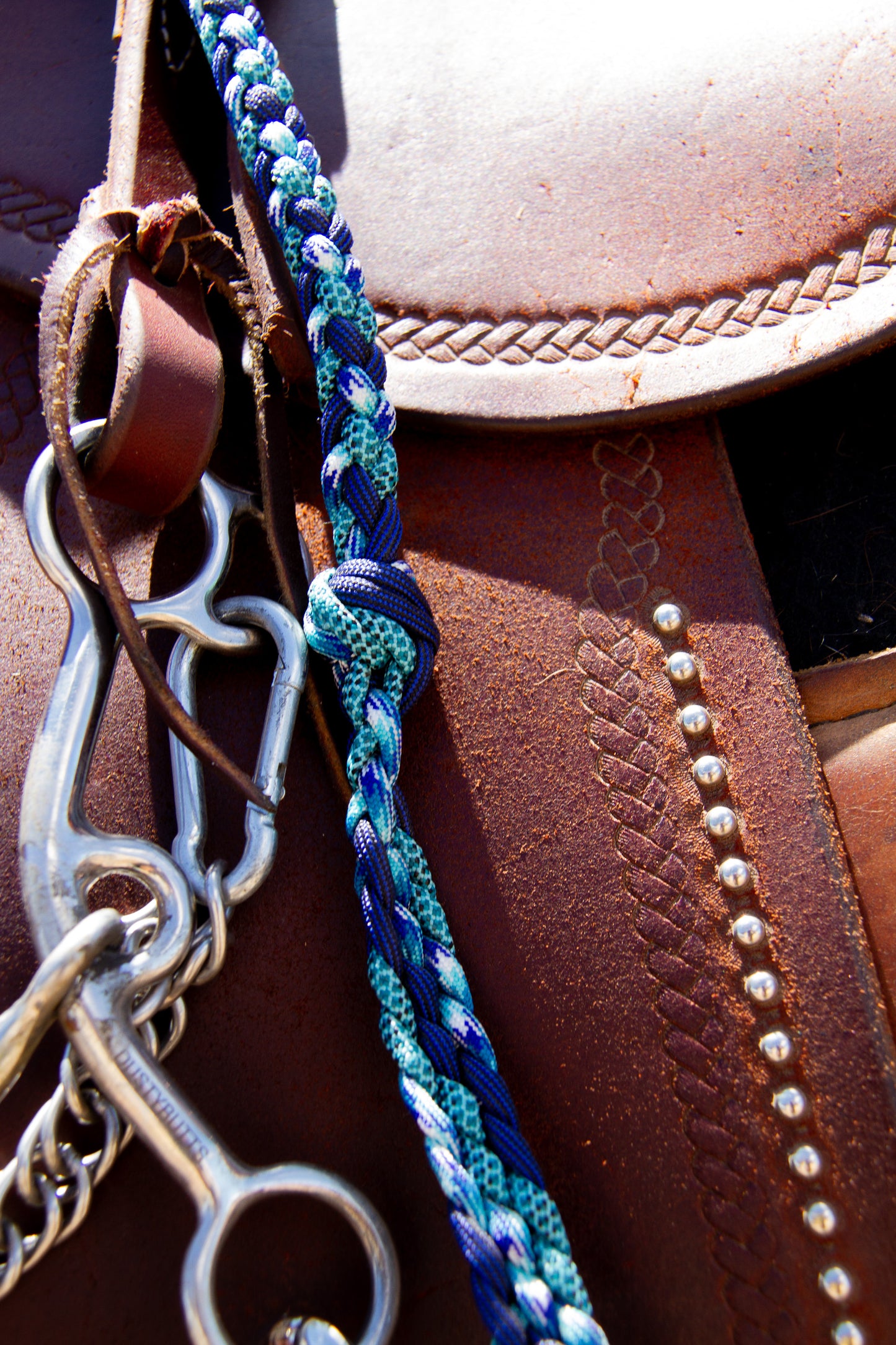 Close-up of a horse bridle with a blue braided reins on a brown leather saddle.