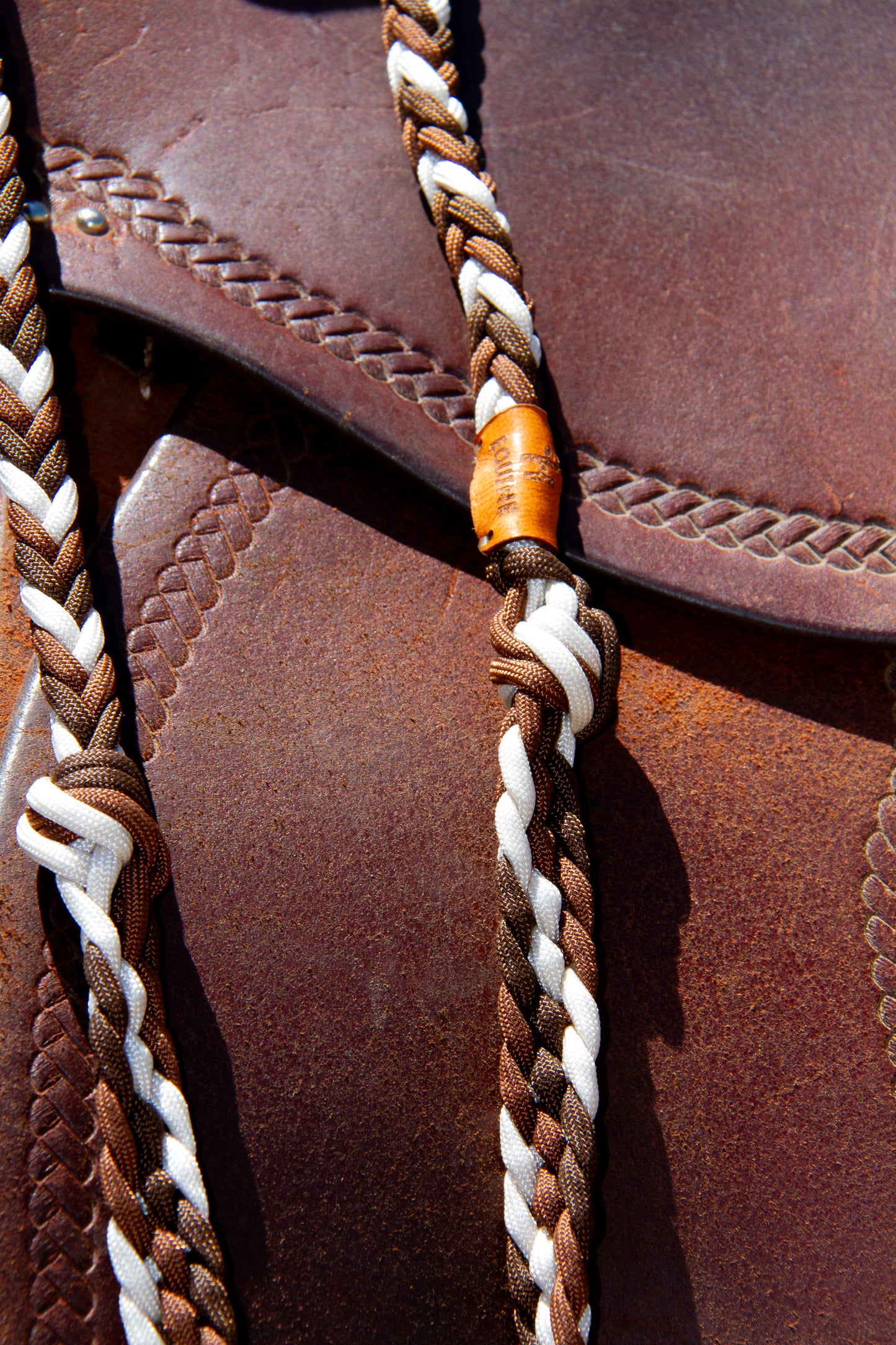 Close-up of a braided leather strap on a brown leather surface