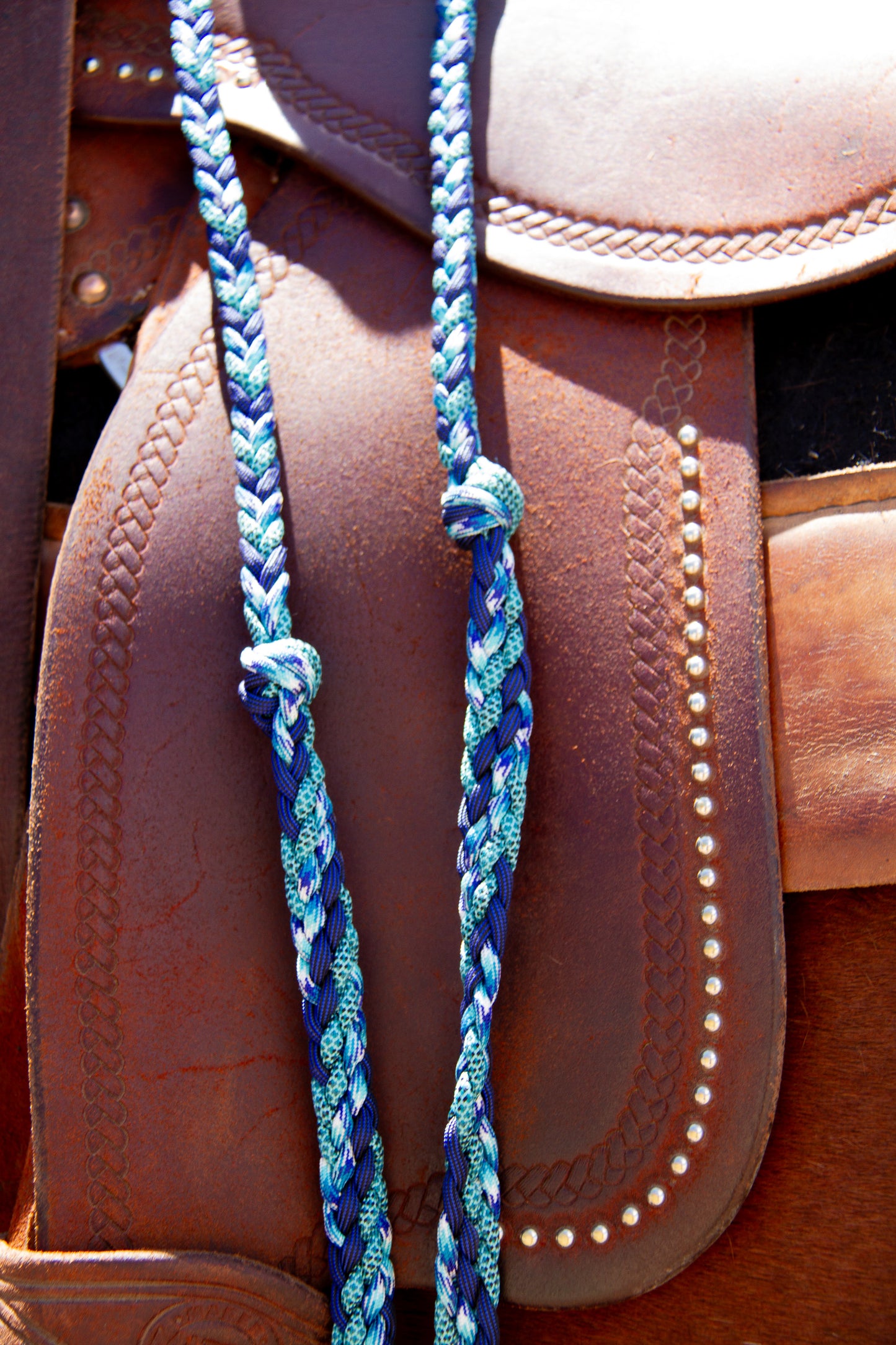 Close-up of a brown leather saddle with blue braided reins.