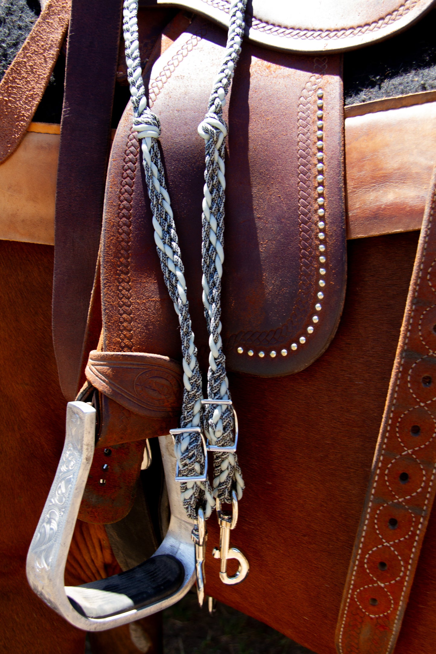 Close-up of a leather saddle with braided reins on saddle in the background
