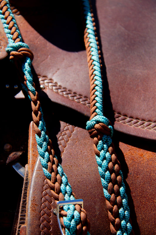 Close-up of a brown leather saddle with braided turquoise and brown reins.