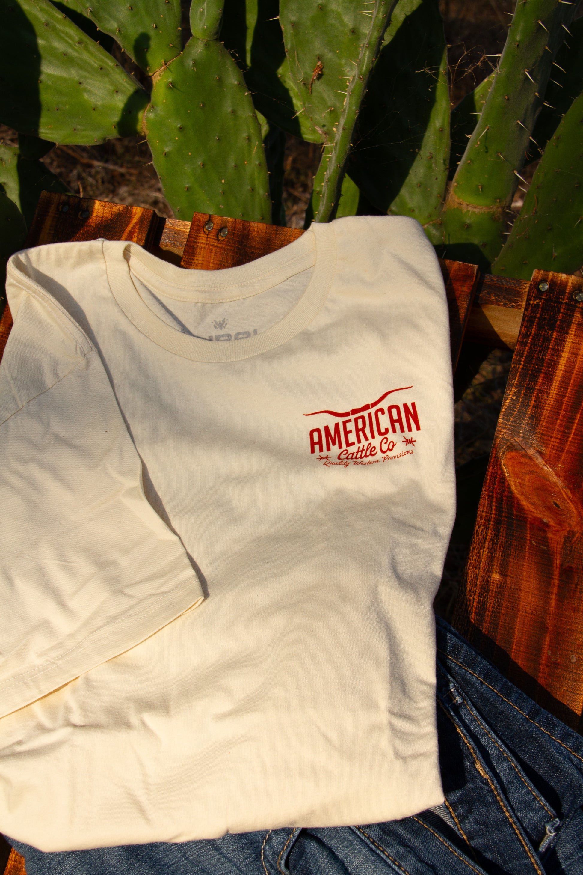 cream t-shirt with red logo on a wooden surface with cacti in the background