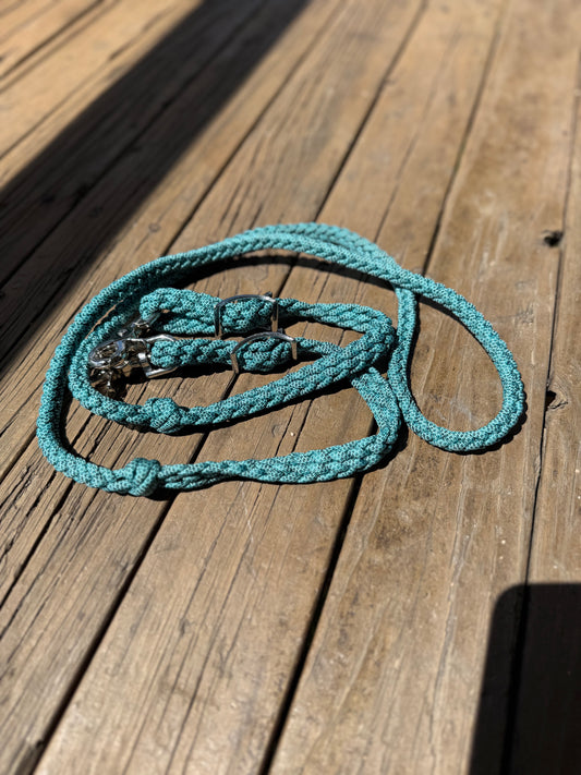 Pattern turquoise nylon roping reins with trigger snaps and flat braid adjustment laid out on timber.