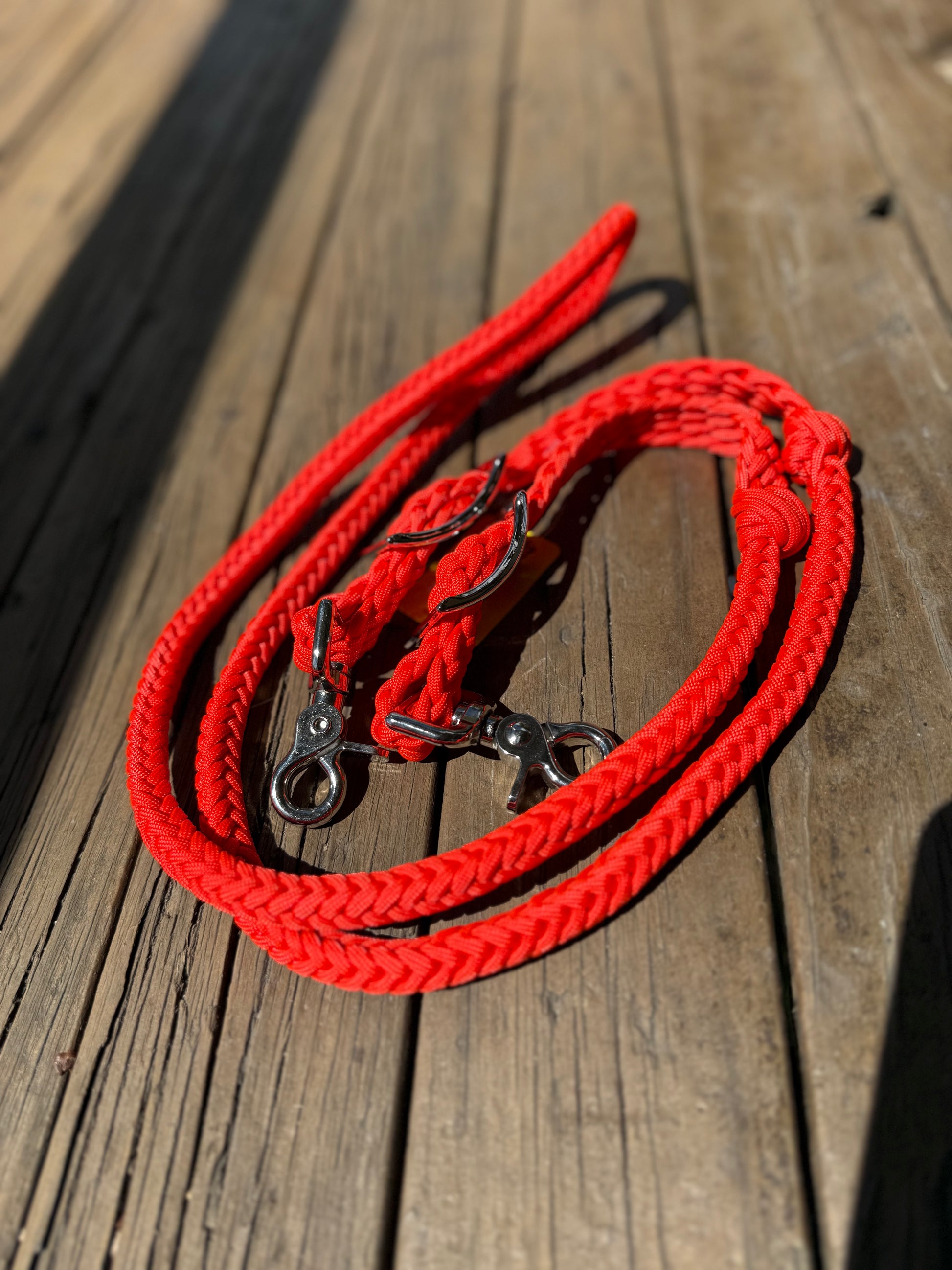 A set of bright orange, hand-braided barrel racing reins laid out on a wooden surface.