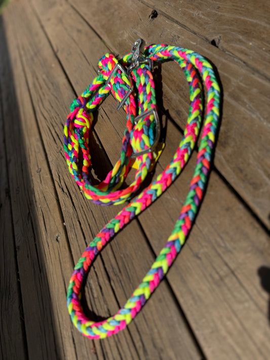 Bright rainbow braided roping reins in pink, yellow, green, blue, and purple with Conway buckles and trigger snaps, displayed on timber decking.