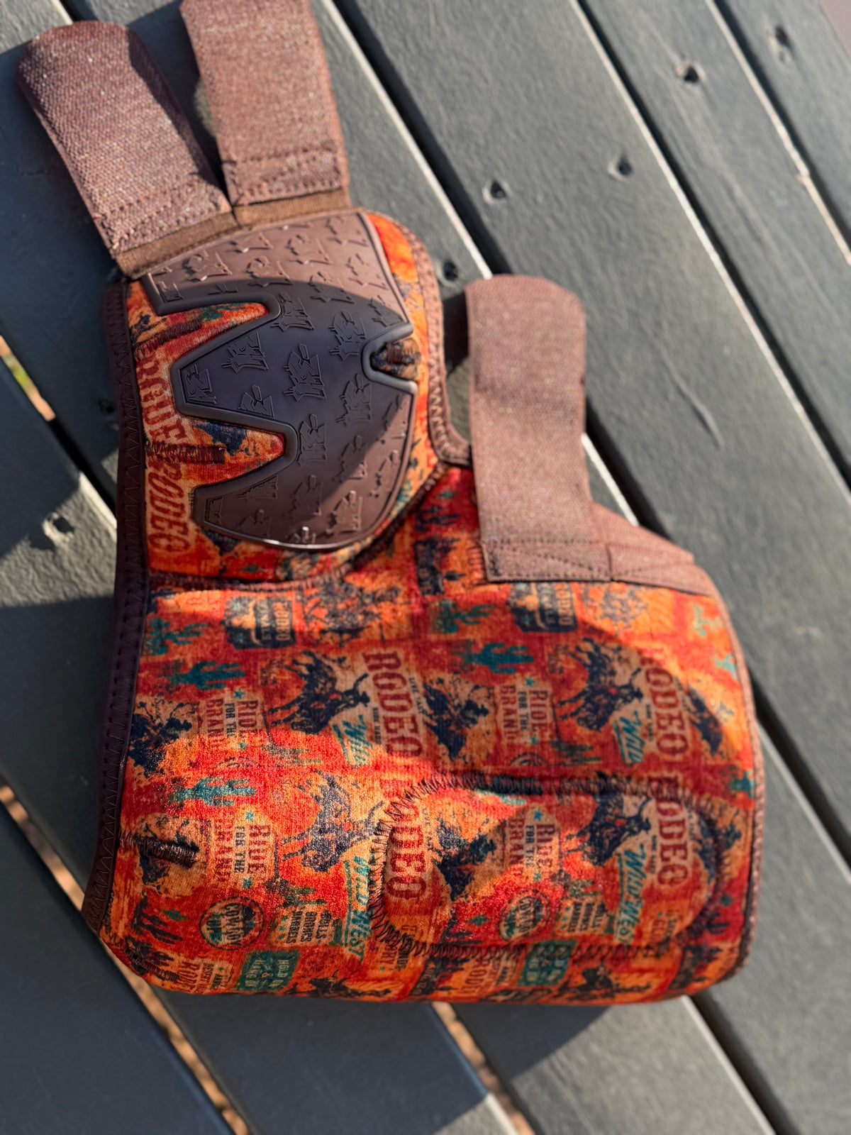 8 Seconds sport boot laid open with orange vintage rodeo print, brown fastening straps and bar3H rubber panel.