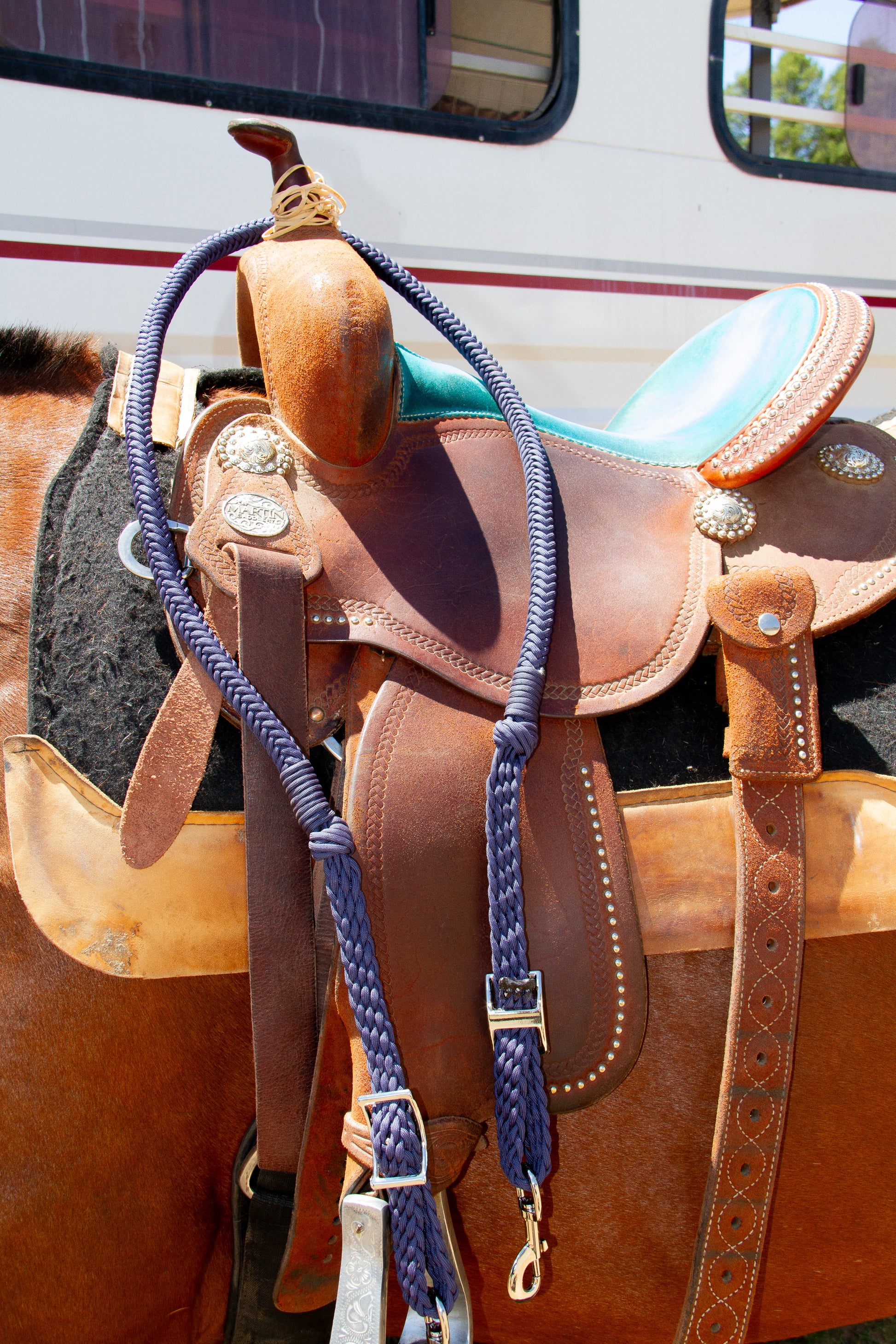 Brown leather saddle with blue reins on a horse, with a vehicle in the background.