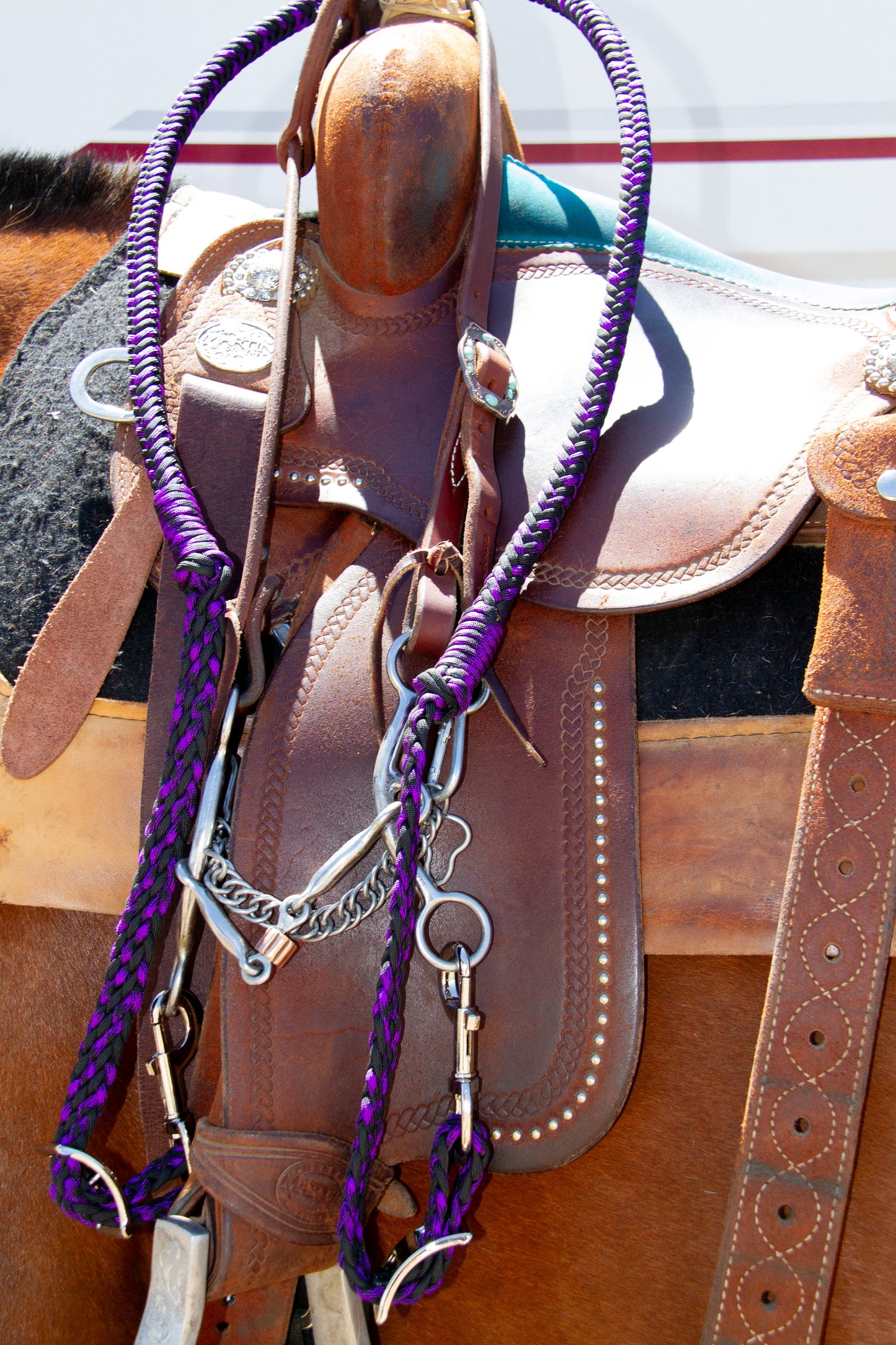 Brown leather saddle with purple reins on a textured surface