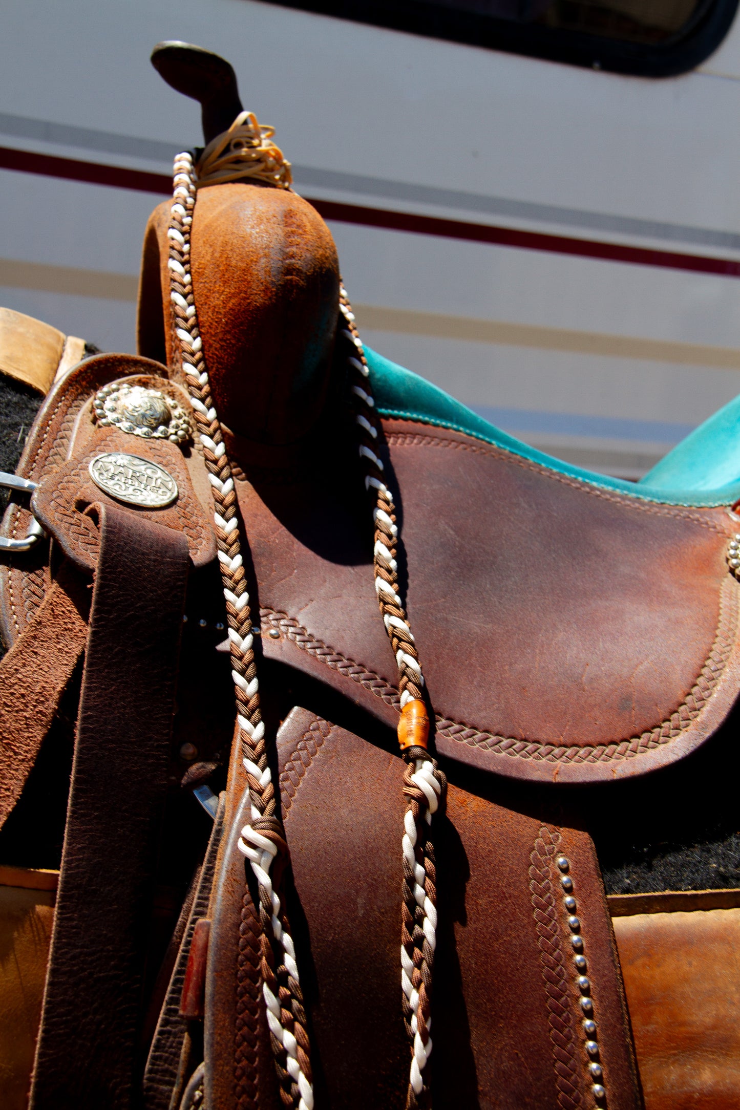 Brown leather saddle with braided reins on a blurred background