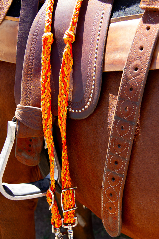 Close-up of a brown leather saddle with an orange braided reins on a blurred background