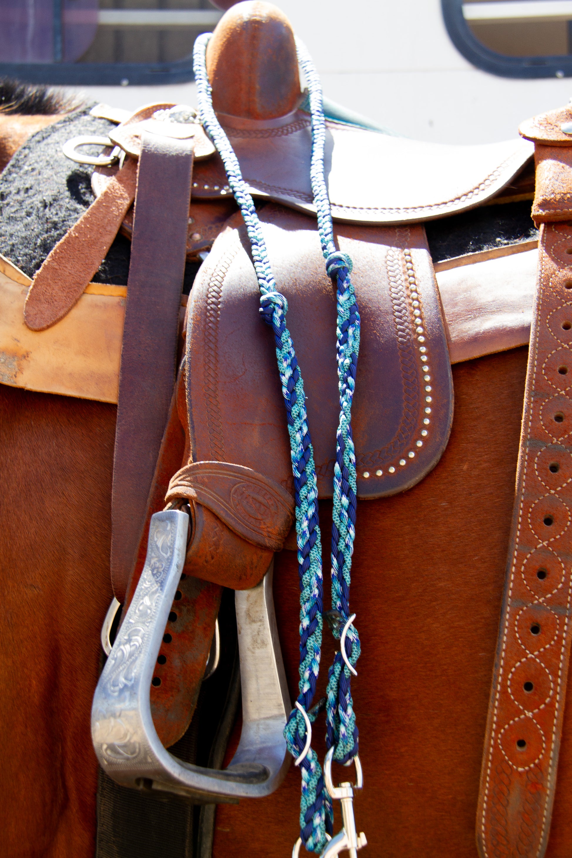 Brown leather saddle with a blue pattern braided reins on a horse, close-up view.