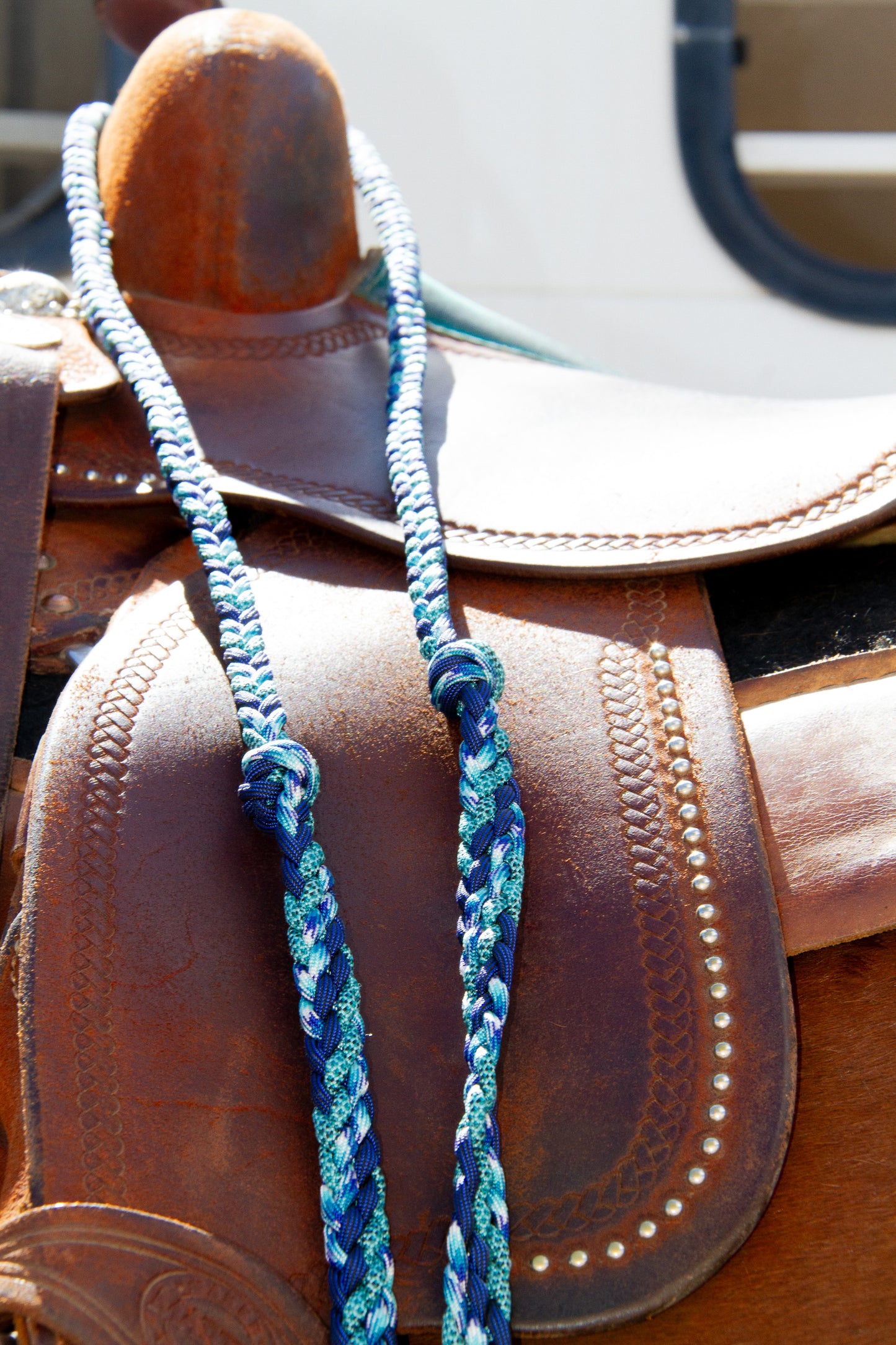 Close-up of a brown leather saddle with blue braided reins on a blurred background