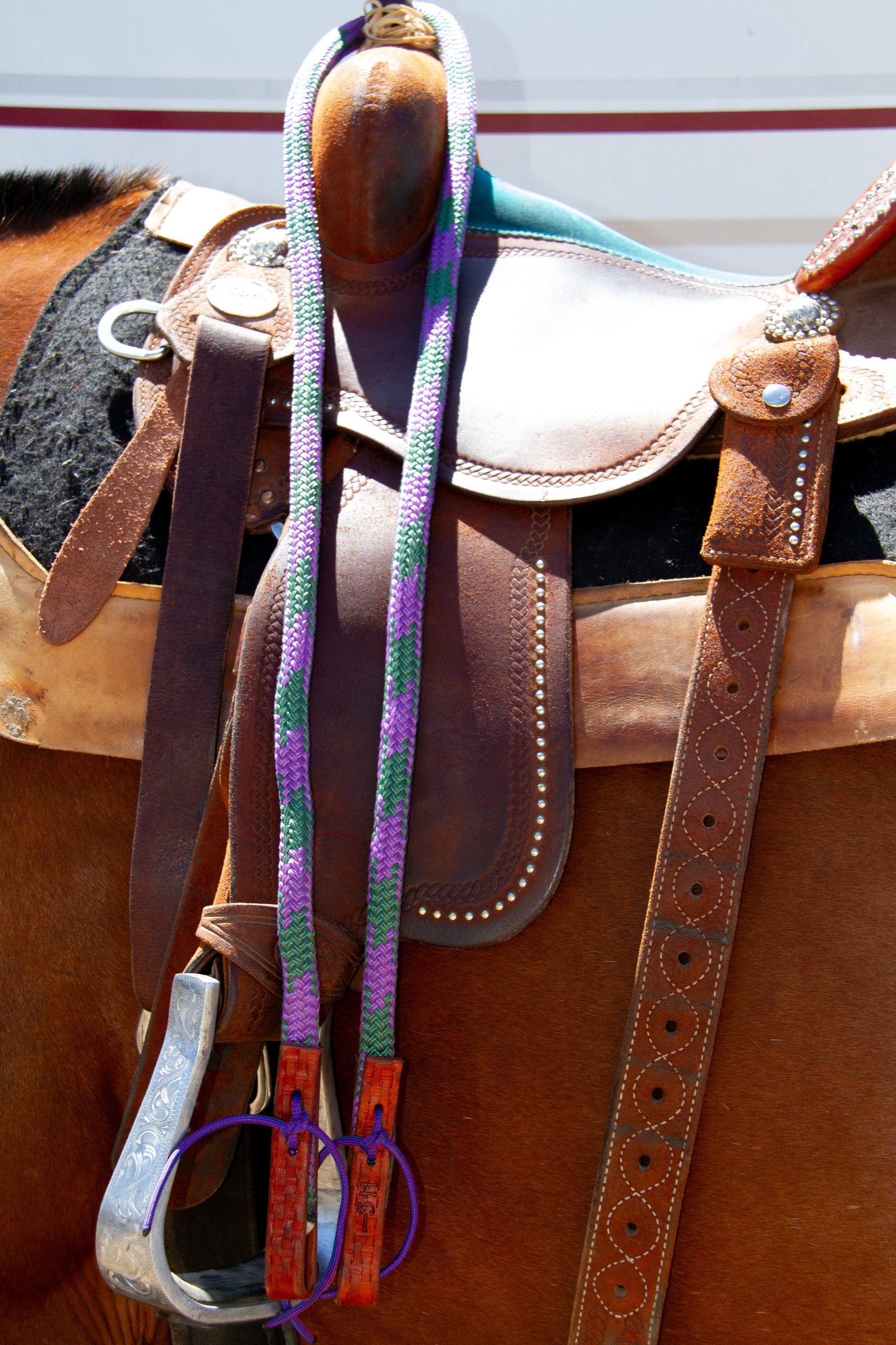Brown leather saddle with colorful reins on a white background