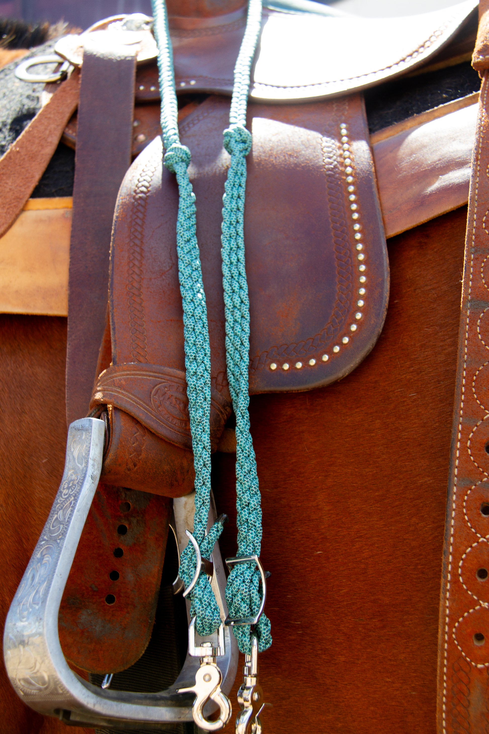 Close-up of a brown leather saddle with a teal reins and metal bit.