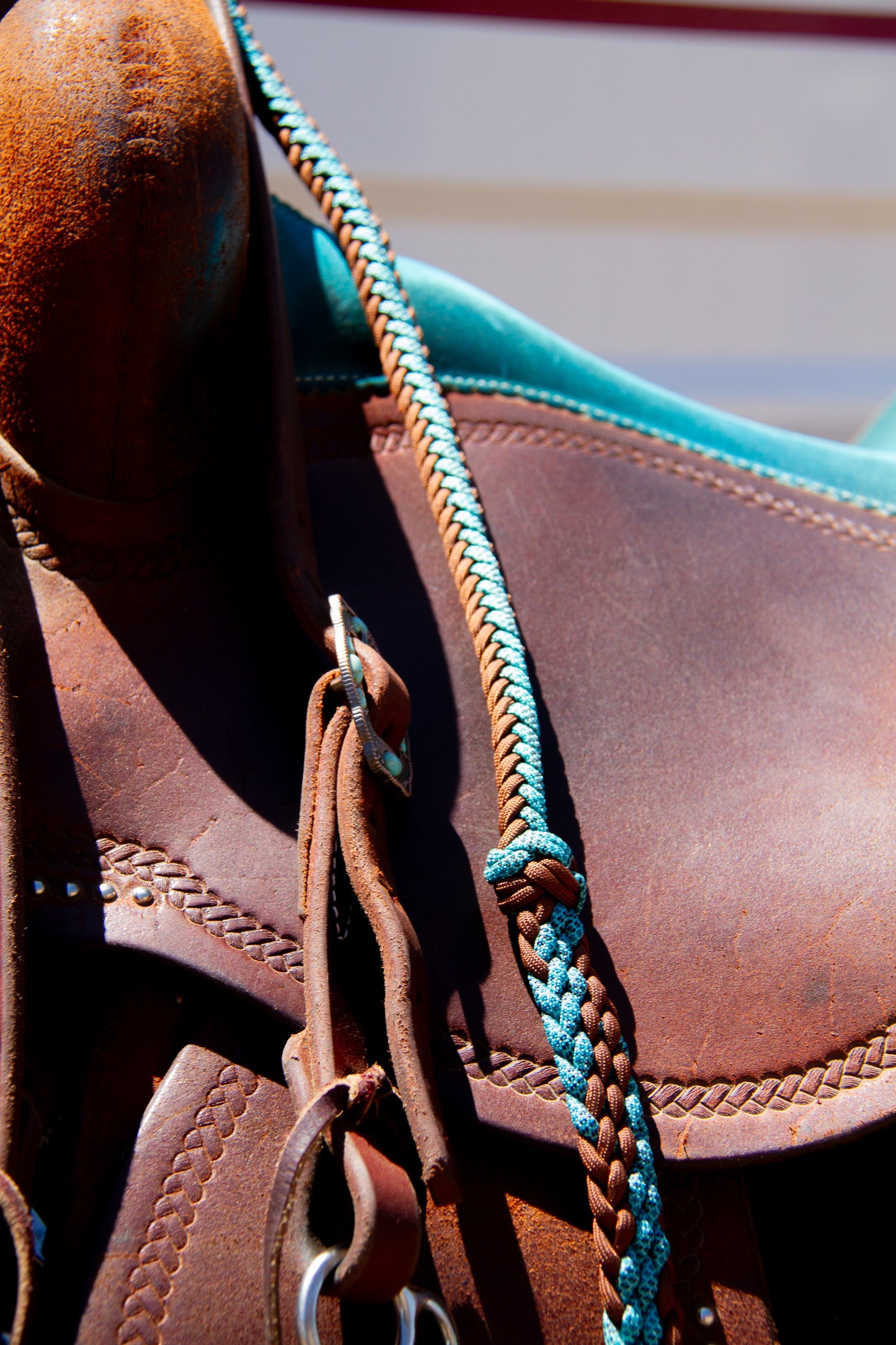 Close-up of a brown leather saddle with a blue braided reins on a striped background
