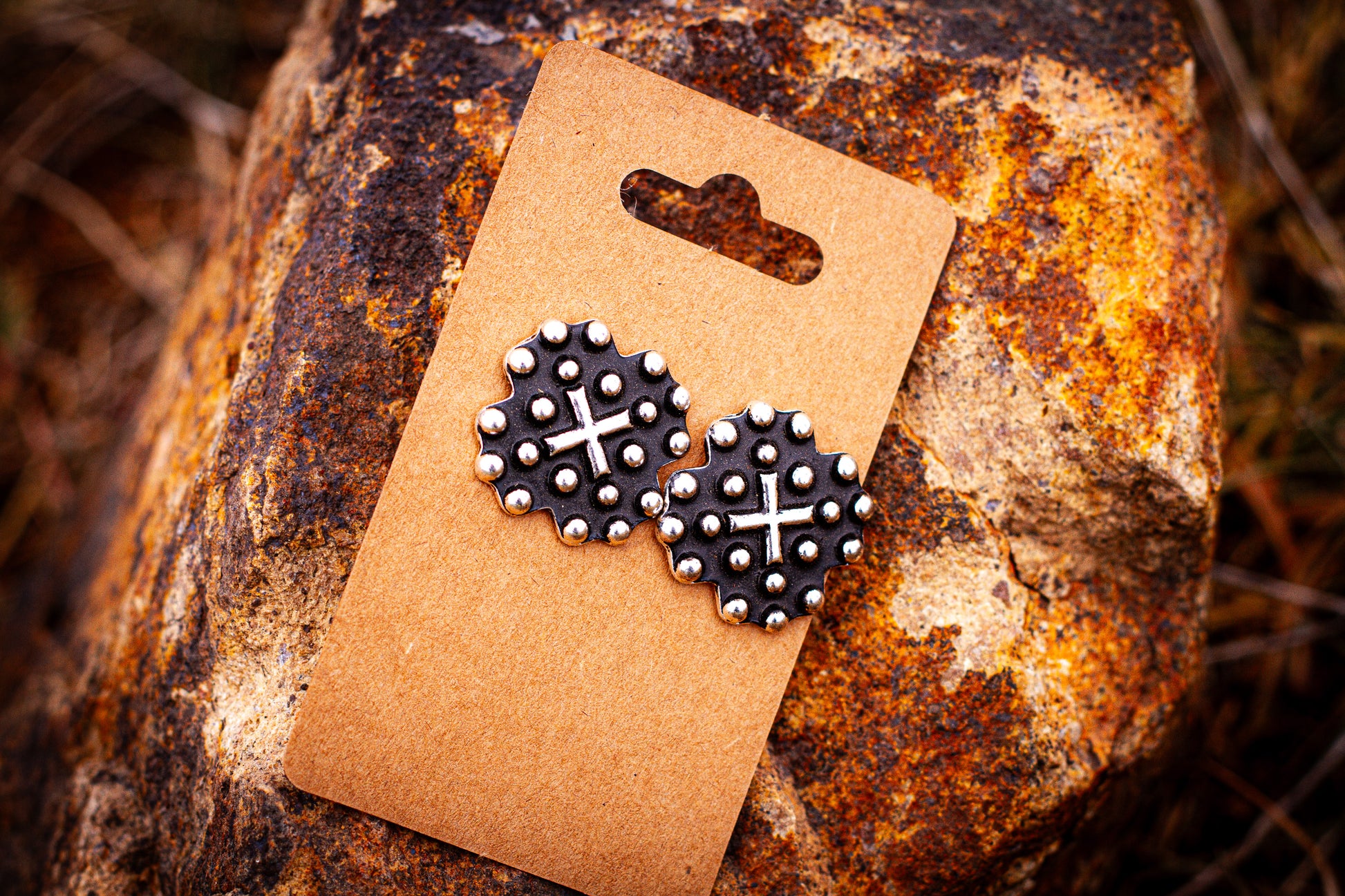 Pair of black and silver earrings on a brown card against a textured stone background