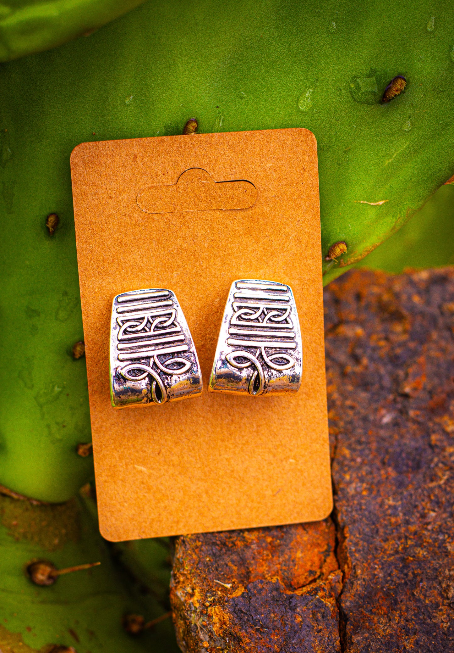 Silver curved bootstitch stud earrings on a brown card with a cactus background