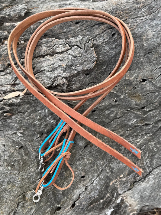 Tan Herman Oak leather split reins with turquoise accents and trigger snaps, coiled on timber