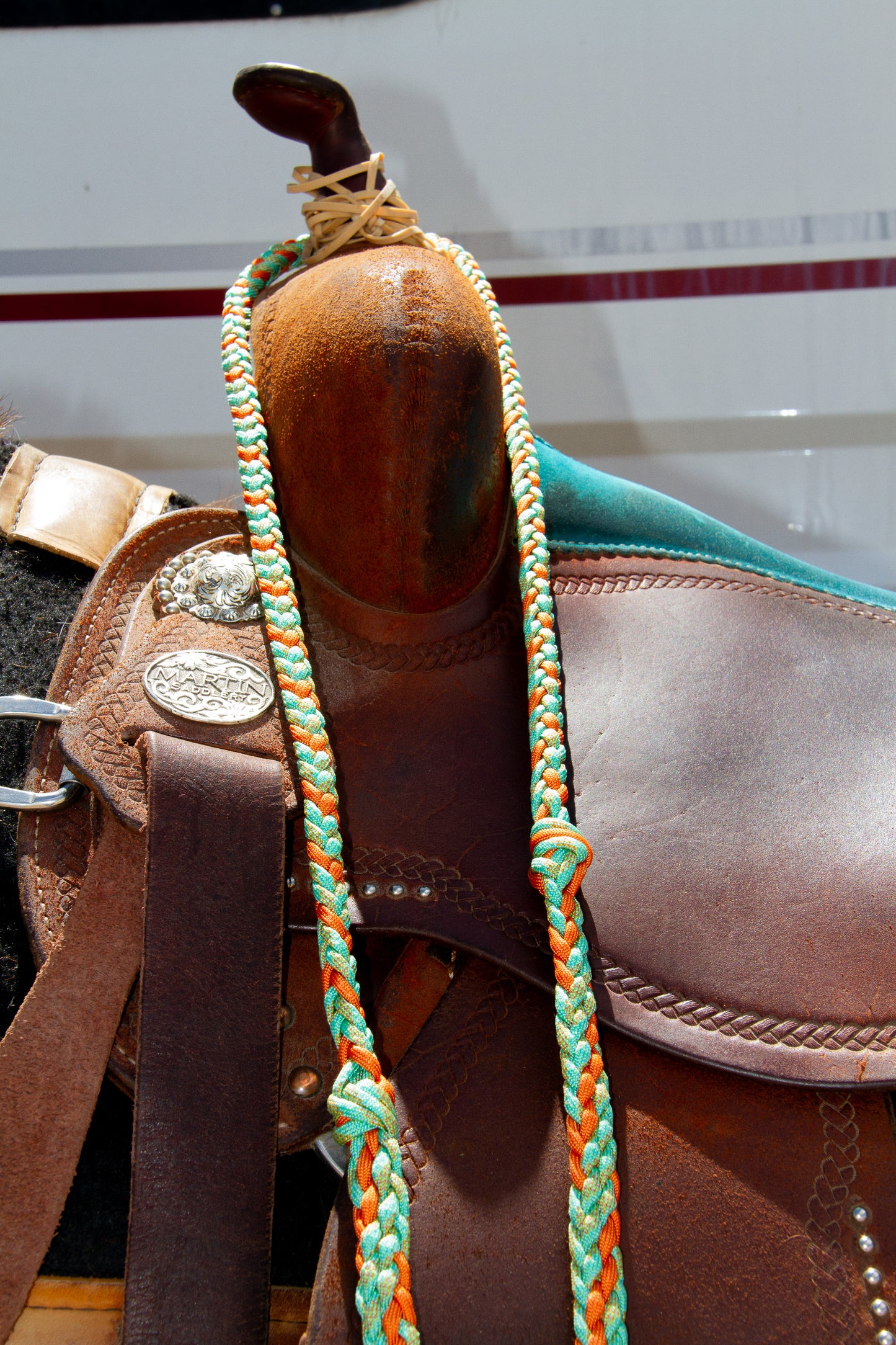 Close-up of a brown leather saddle with a braided rein on a white background