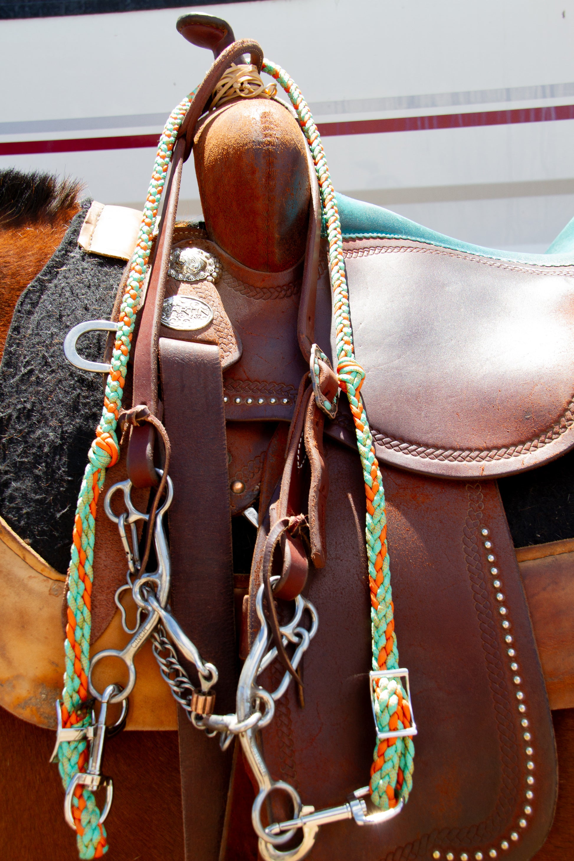 Brown leather saddle with a bridle and colorful reins on a horse.