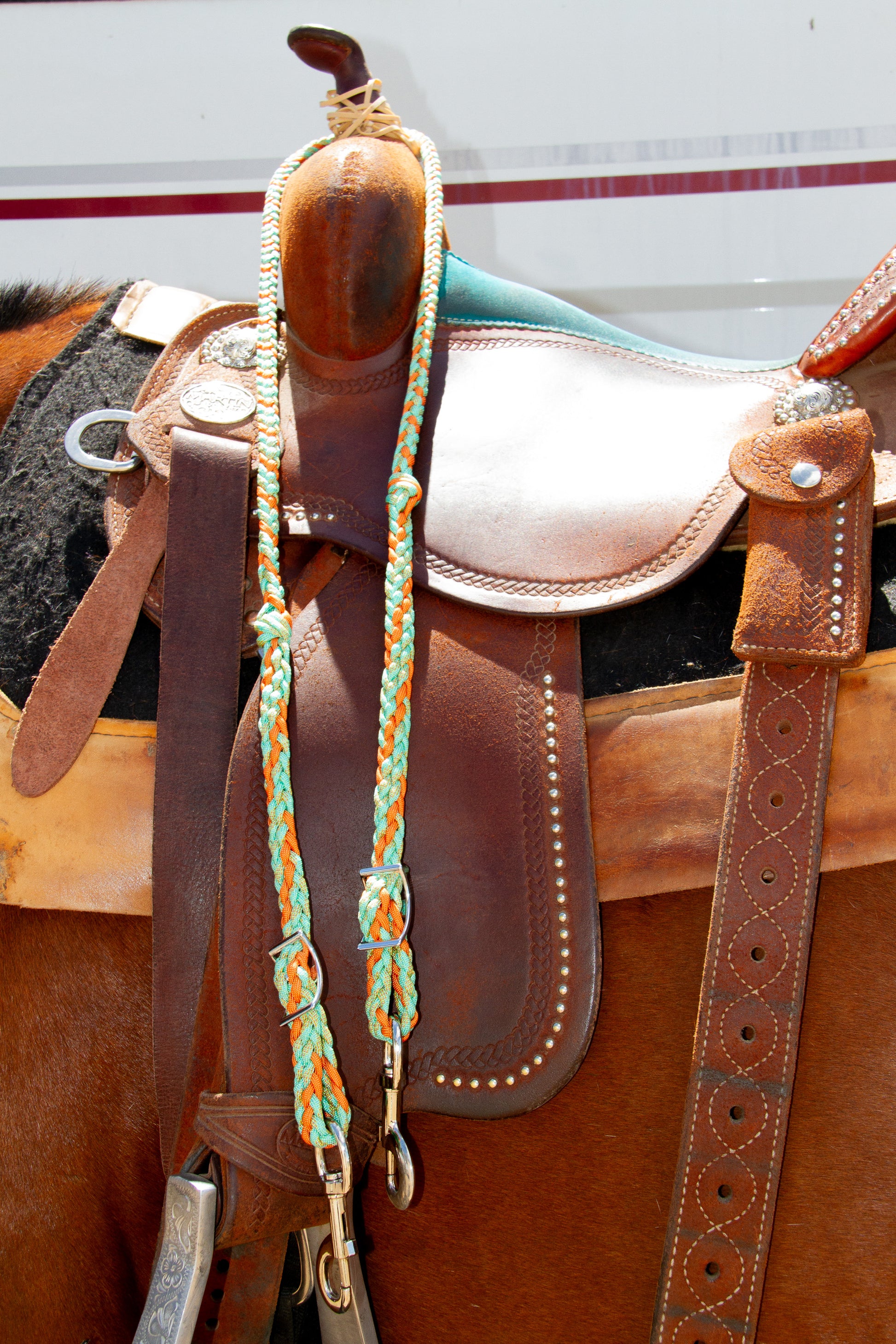 Close-up of a brown leather saddle with a colorful braided reins on a horse.