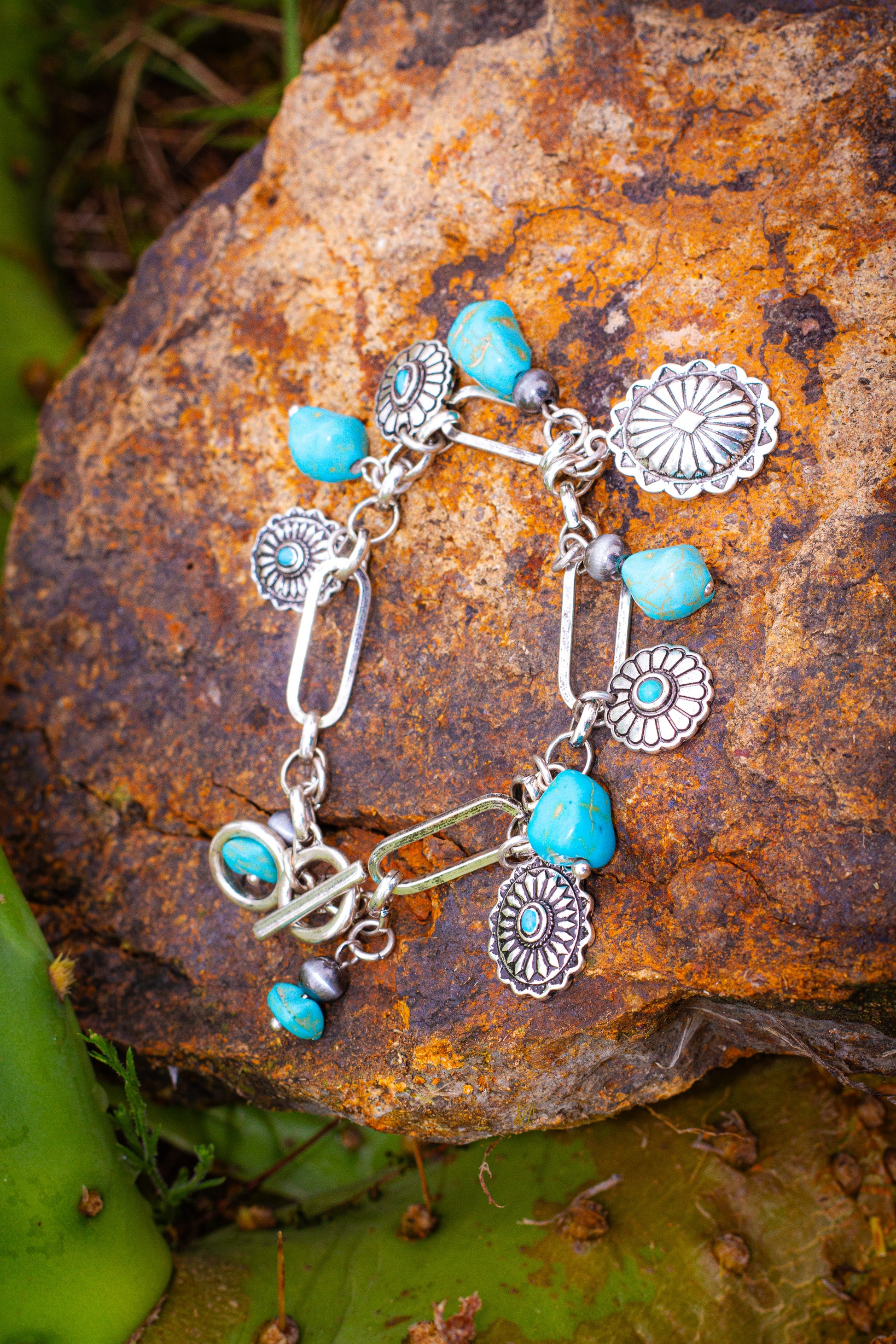 Silver charm bracelet with turquoise stones on a textured rock surface