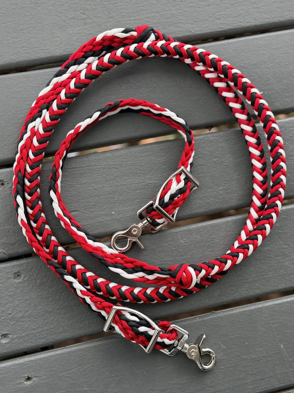 Black, white and red hand-braided stabiliser reins coiled on grey decking, showing knots, conway buckles and trigger snaps