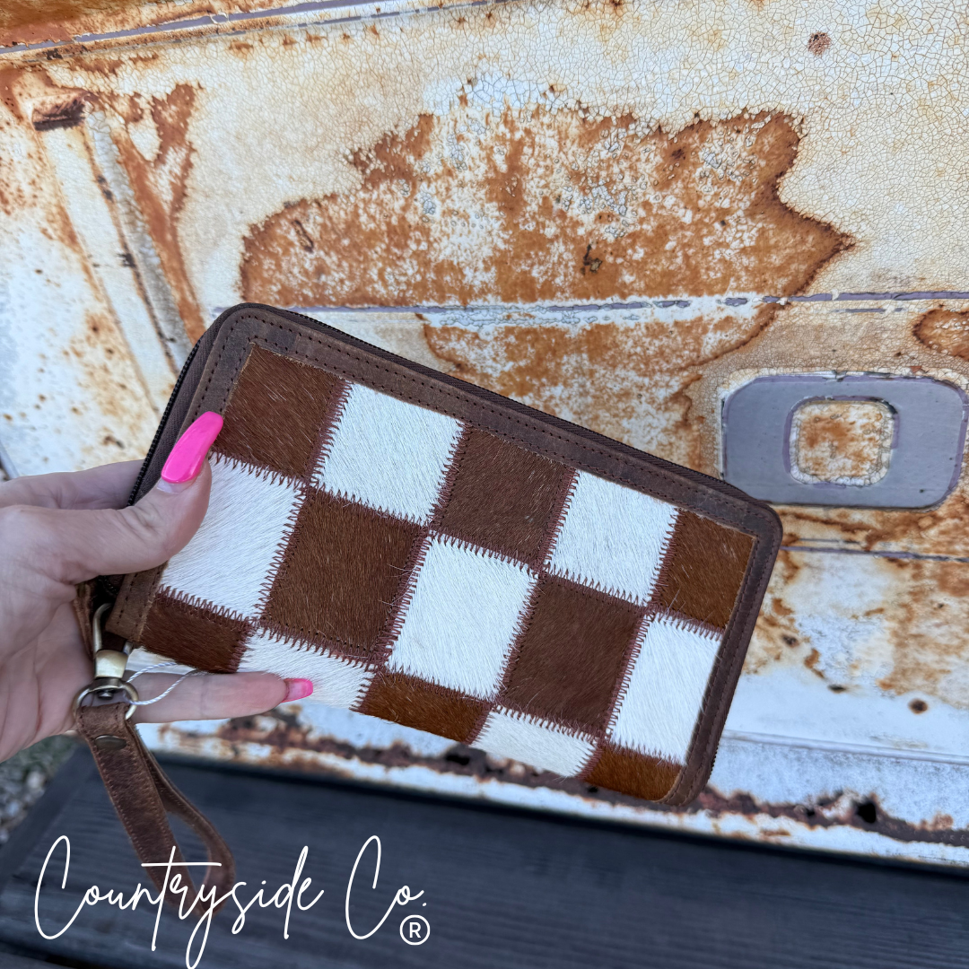 Brown and white checkered wallet held by a hand against a rusty metal background with 'Countryside Co' branding.