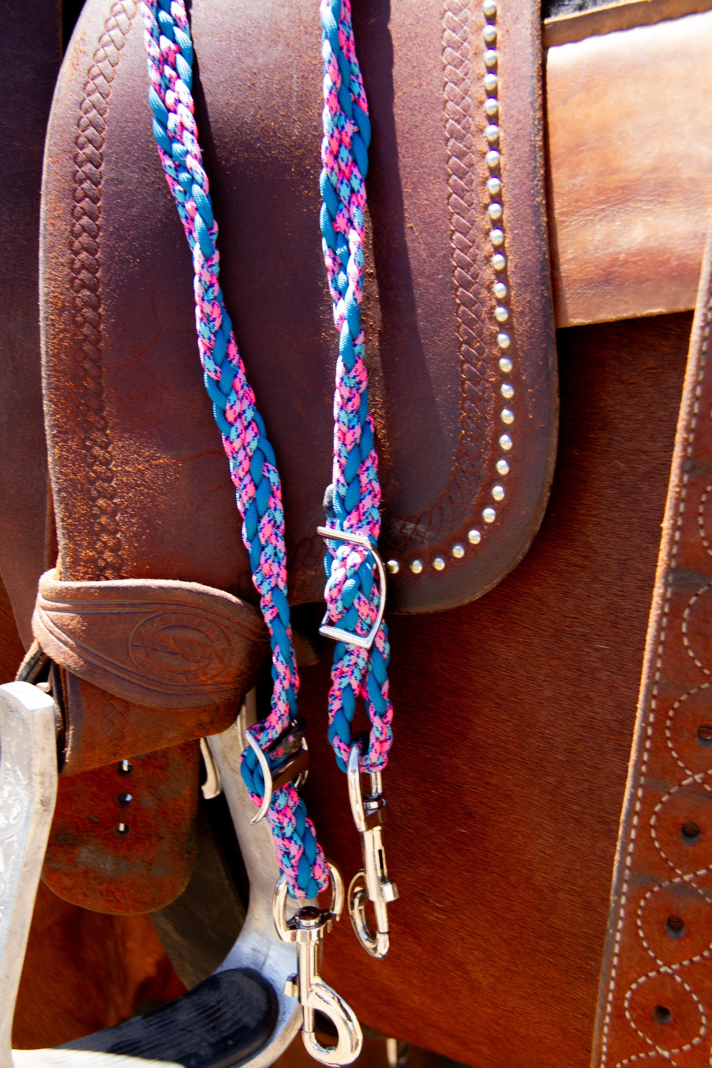 Close-up of a brown leather saddle with a colorful braided reins.