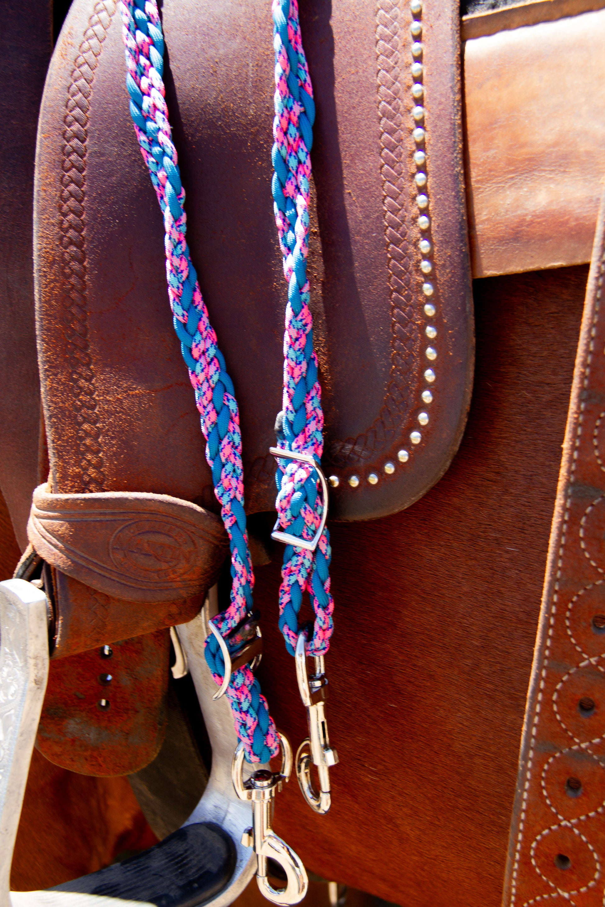 Close-up of a brown leather saddle with a colorful braided reins.