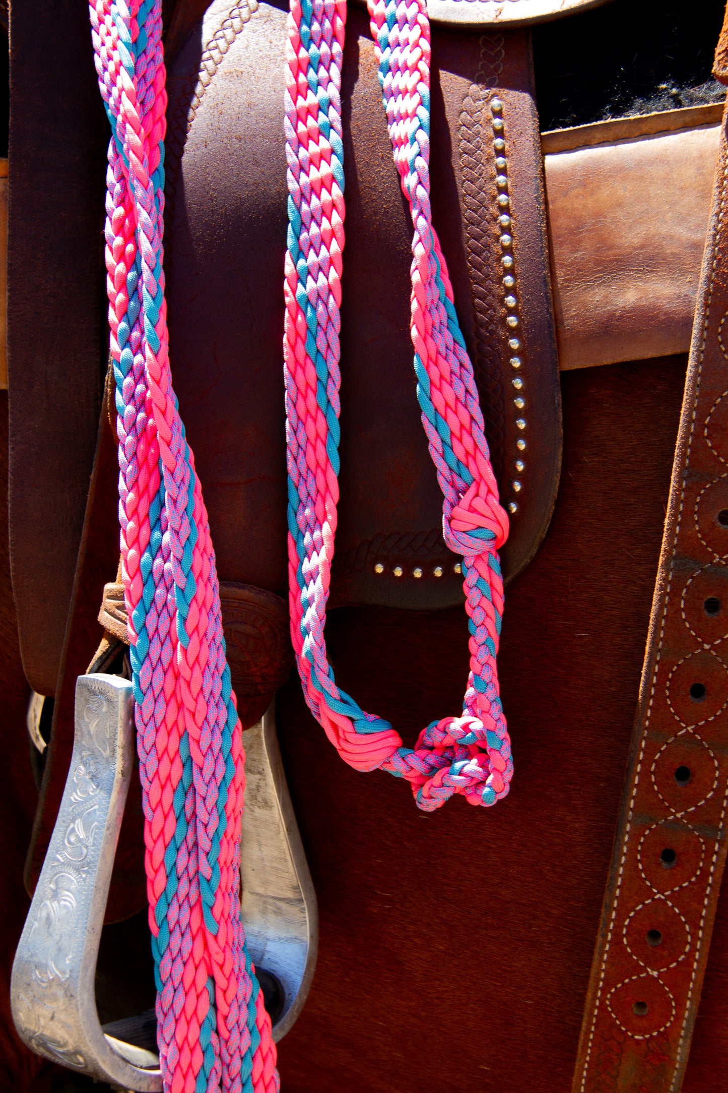 Close-up of a brown leather saddle with pink and blue braided reins.