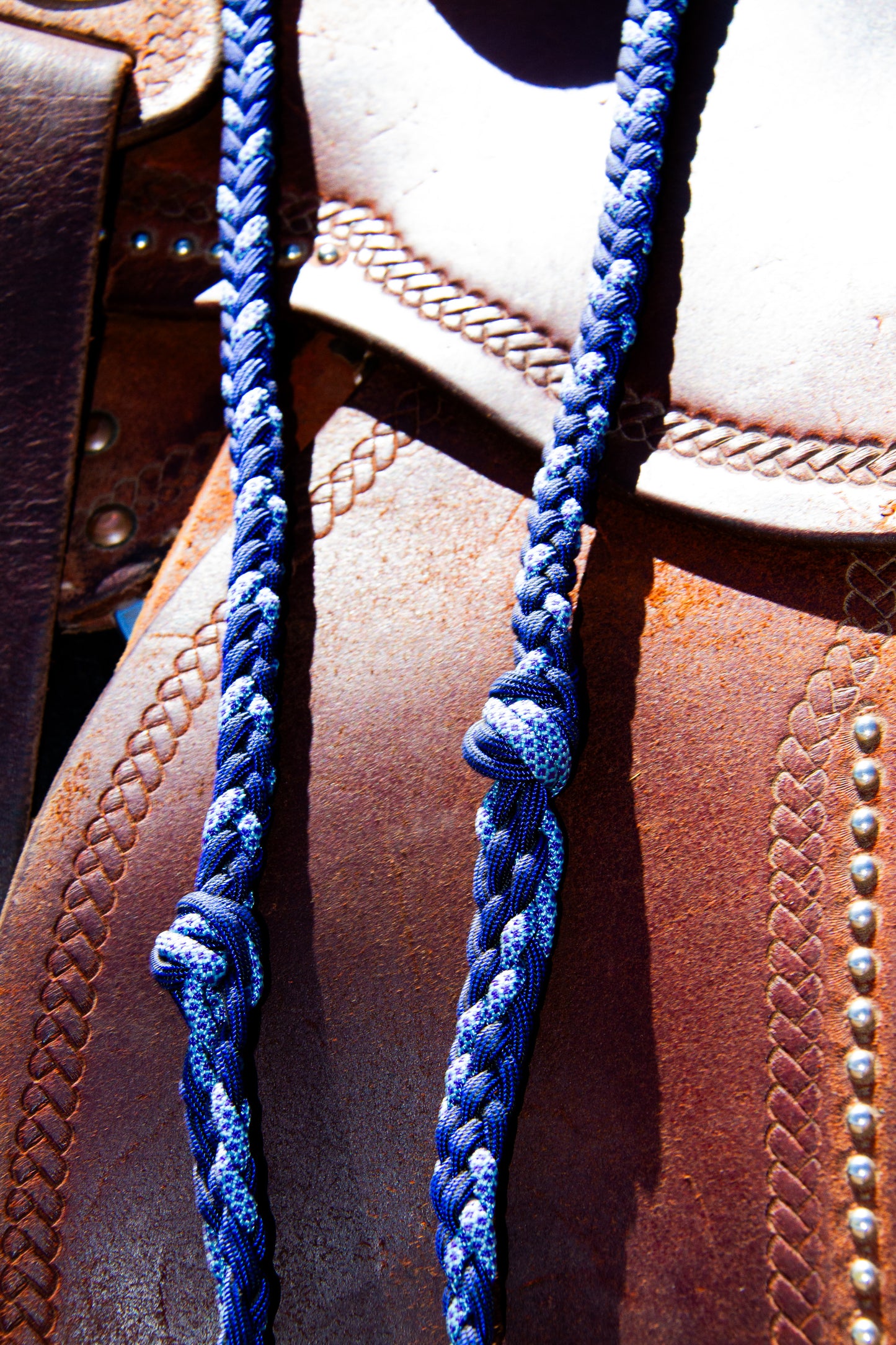 Close-up of a brown leather saddle with blue braided reins