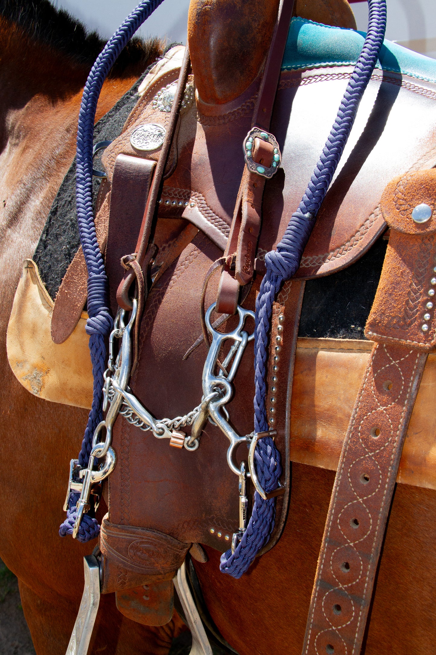 Close-up of a horse saddle with bridle and reins on a brown leather saddle pad.