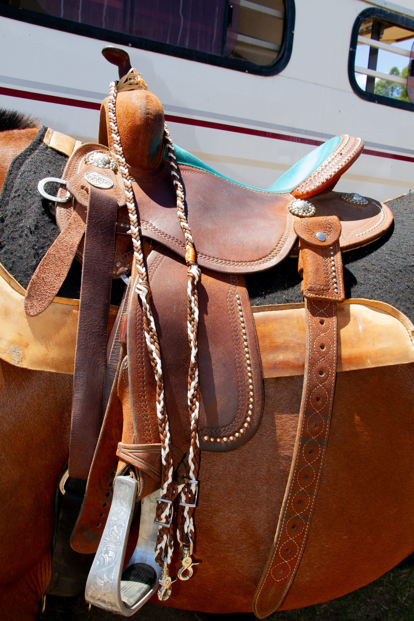 Brown leather saddle with neutral braided reins holder on a trailer background