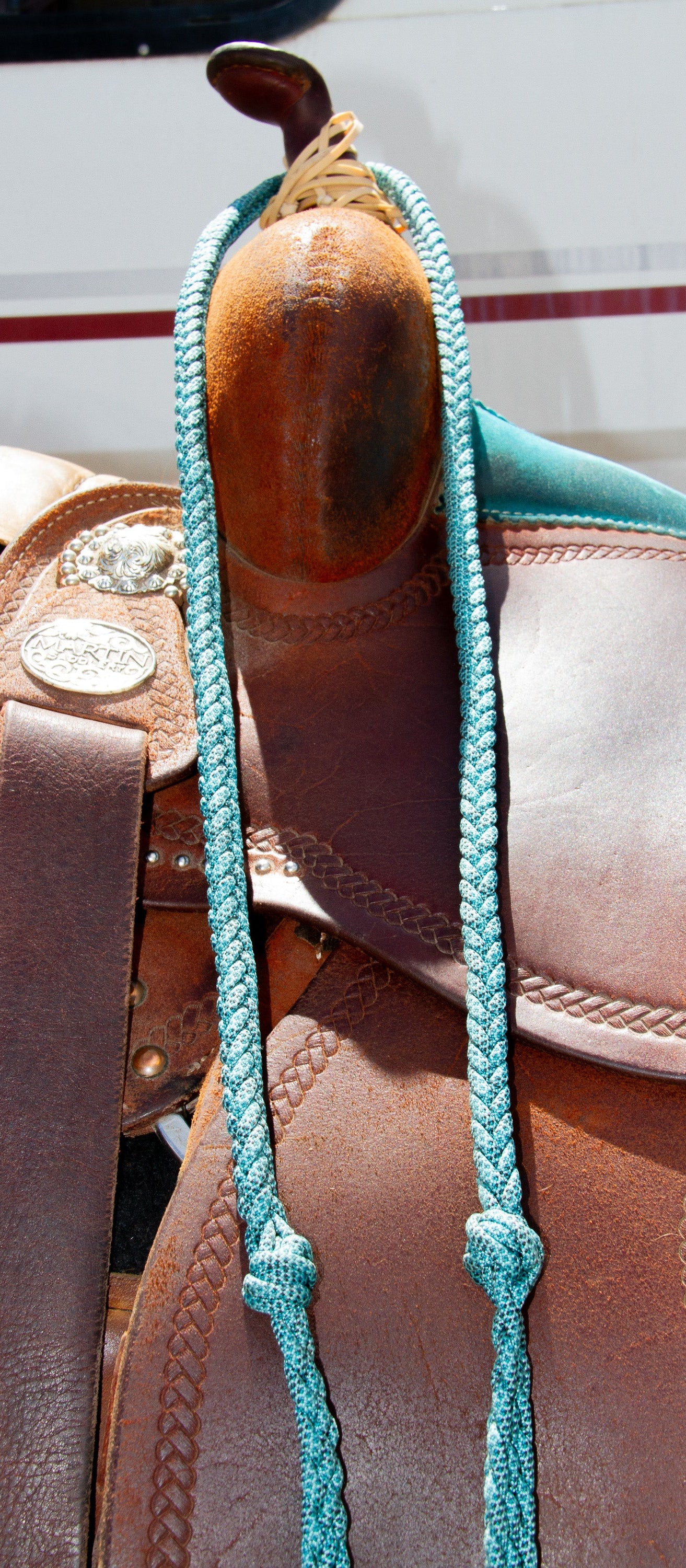 Close-up of a brown leather saddle with turquoise reins on a blurred background